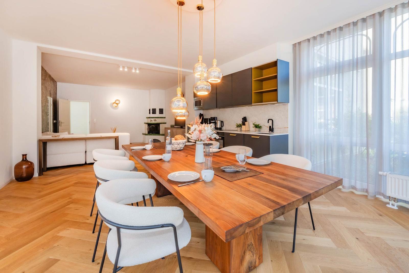 Essbereich mit Holztisch, weißen Stühlen und moderner Küche im Hintergrund.