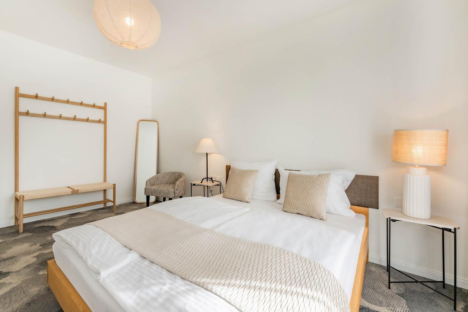 Schlafzimmer mit Bett, Nachttisch, Kleiderständer und Spiegel.