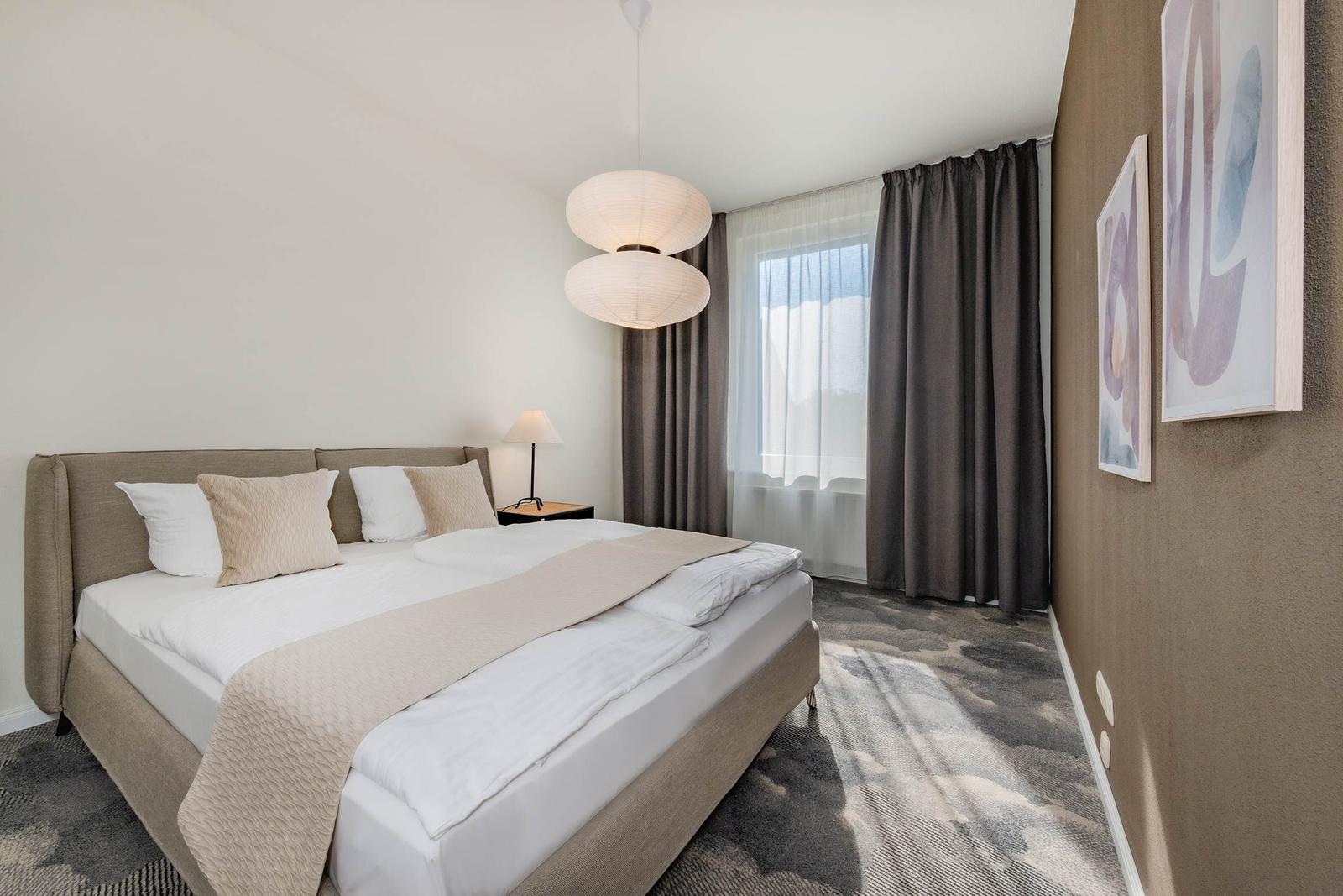 Schlafzimmer mit Doppelbett, Fenster und moderner Beleuchtung.