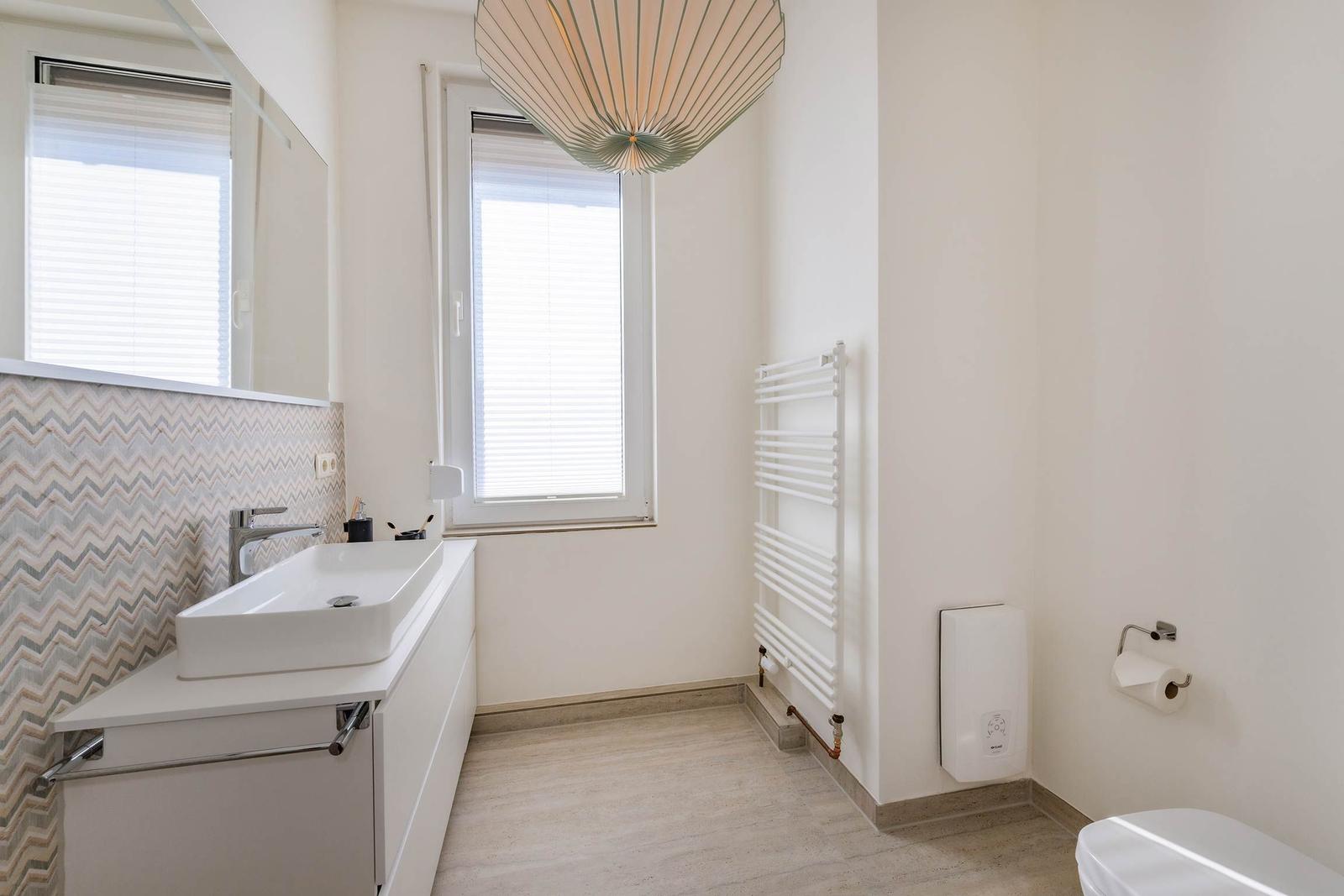 Badezimmer mit Waschbecken, Spiegel, Fenster und Heizkörper.