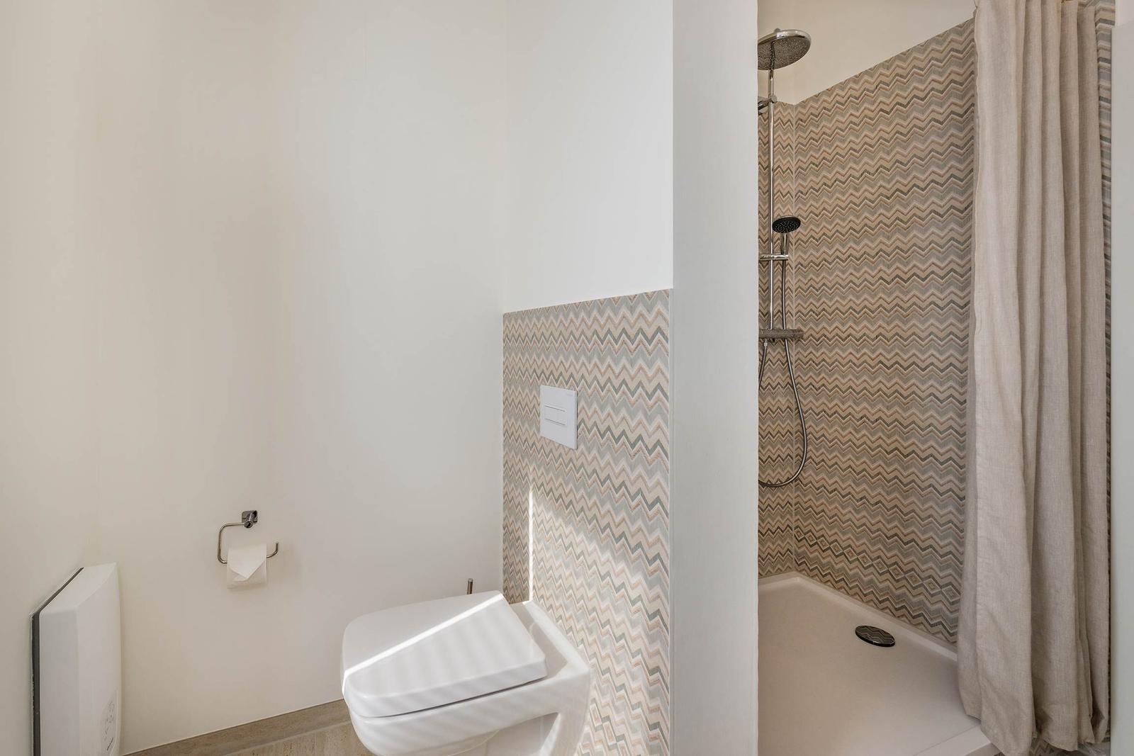 Badezimmer mit Dusche und WC. Duschwand mit Muster. Beige Vorhang.