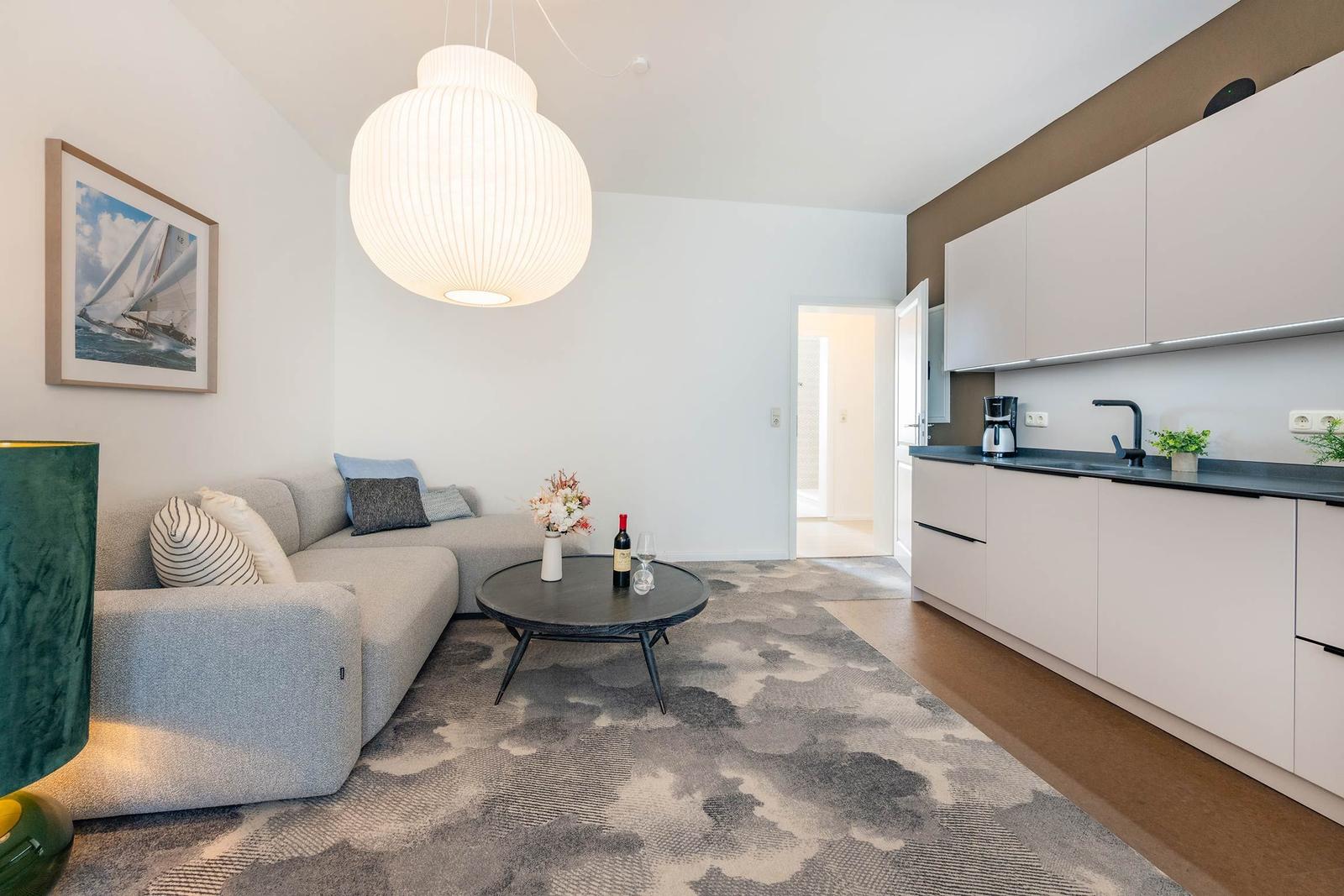 Wohn- und Küchenbereich mit Sofa, Tisch und moderner Beleuchtung.