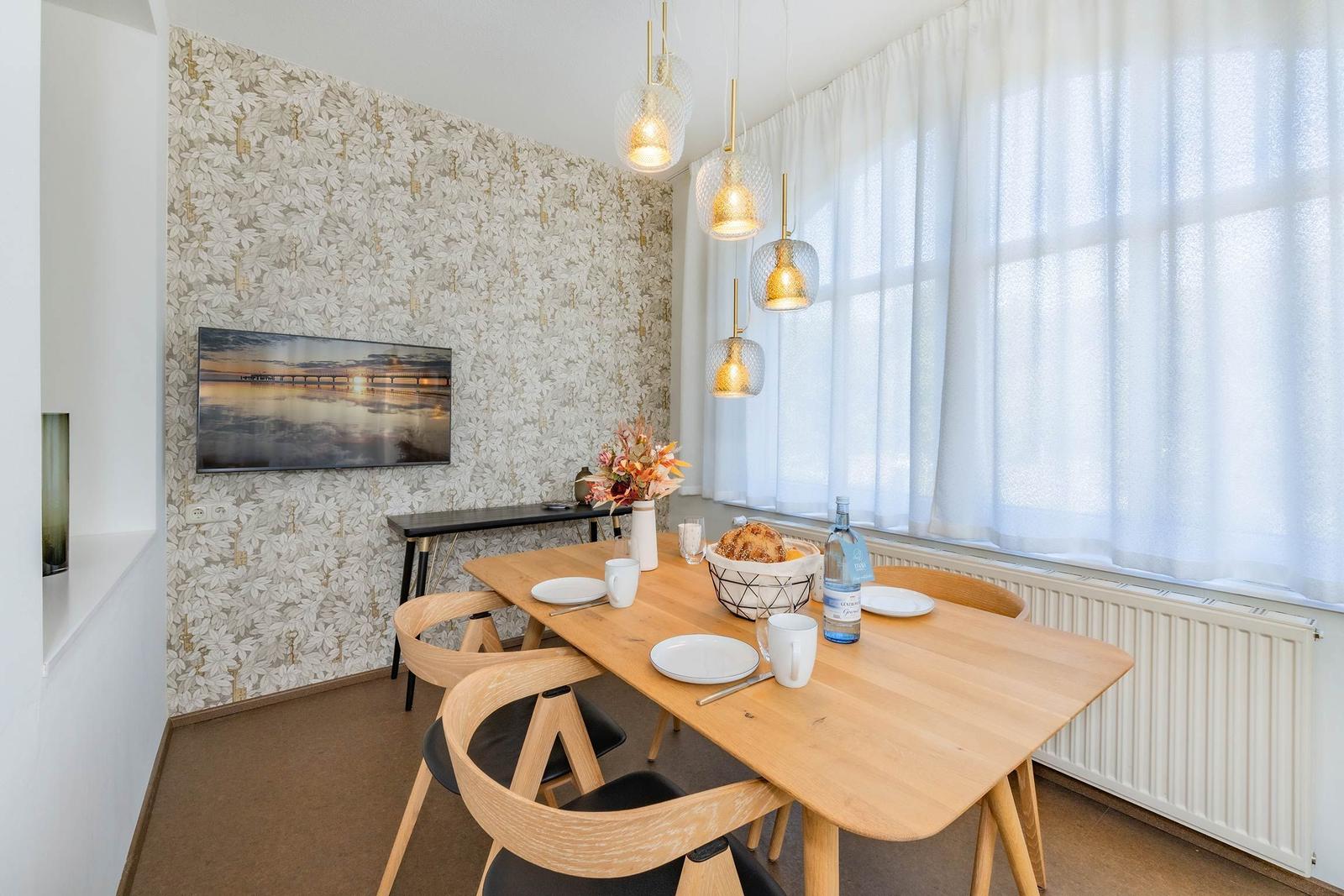 Esszimmer mit Holztisch, Stühlen und Fenster. Wand mit Tapete und Bild.