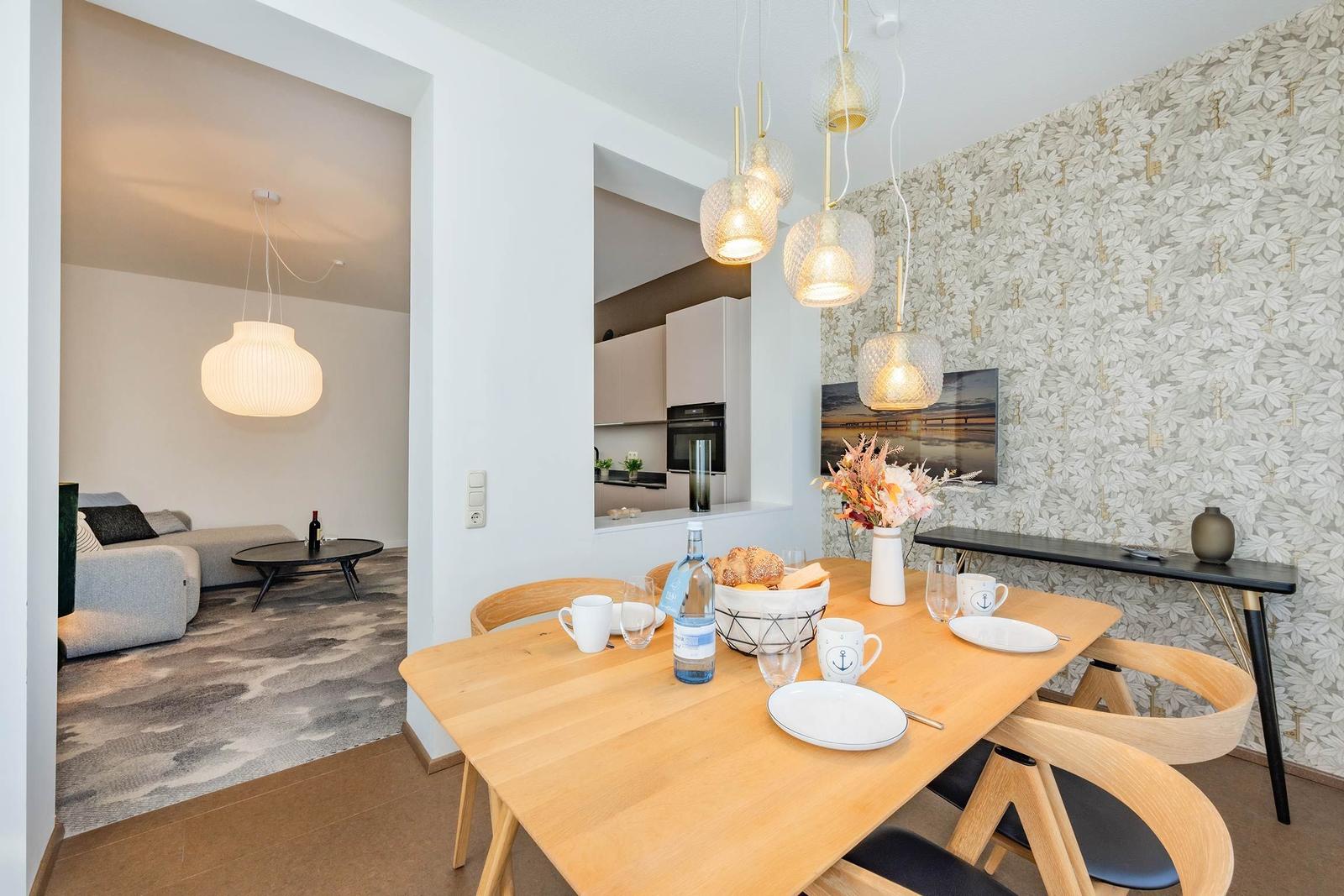 Essbereich mit Holztisch, Stühlen und dekorativer Tapete. Küche und Wohnzimmer sind sichtbar.