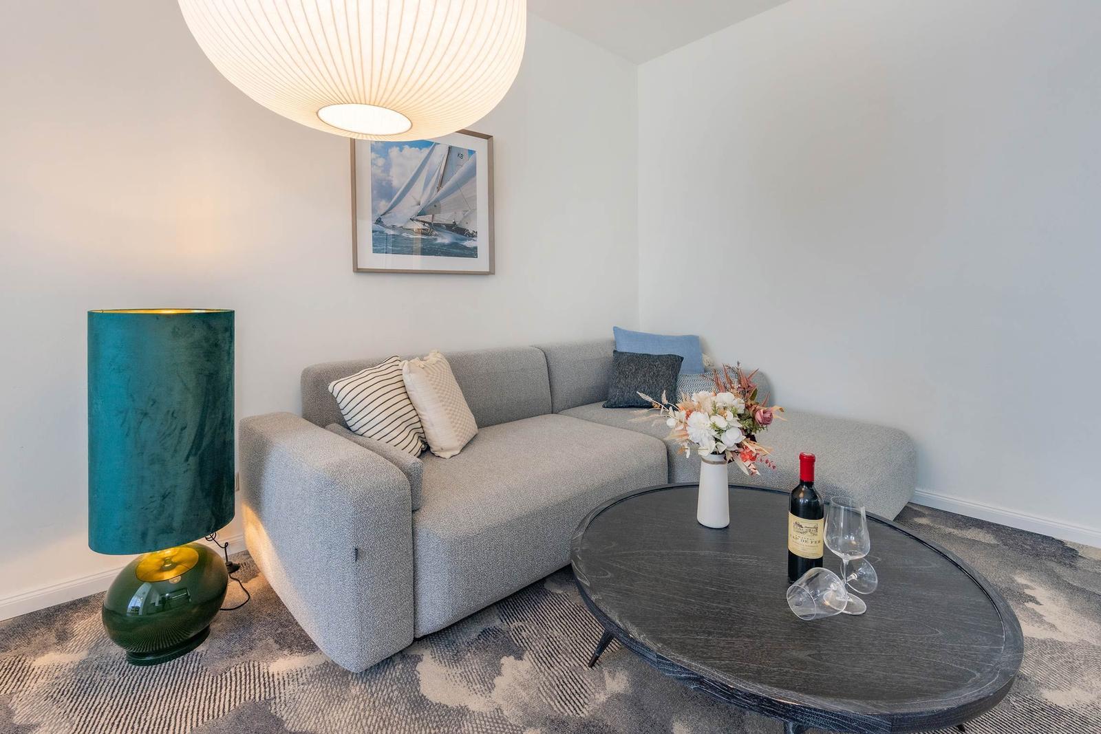 Ein Wohnzimmer mit grauem Sofa, runden Tisch und Stehlampe.