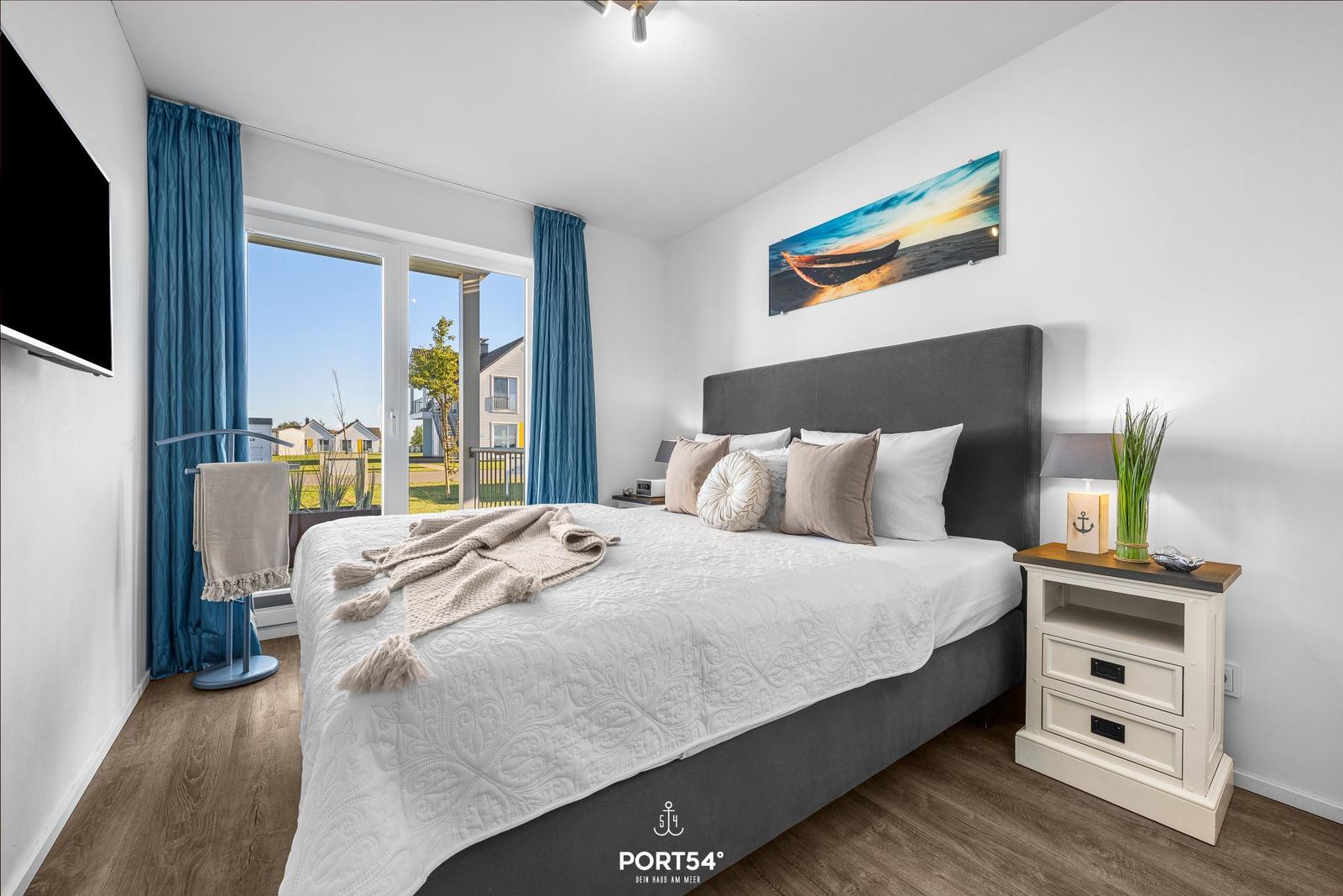 Schlafzimmer mit Bett, Nachttisch und TV. Fenster mit Blick auf Außengelände.