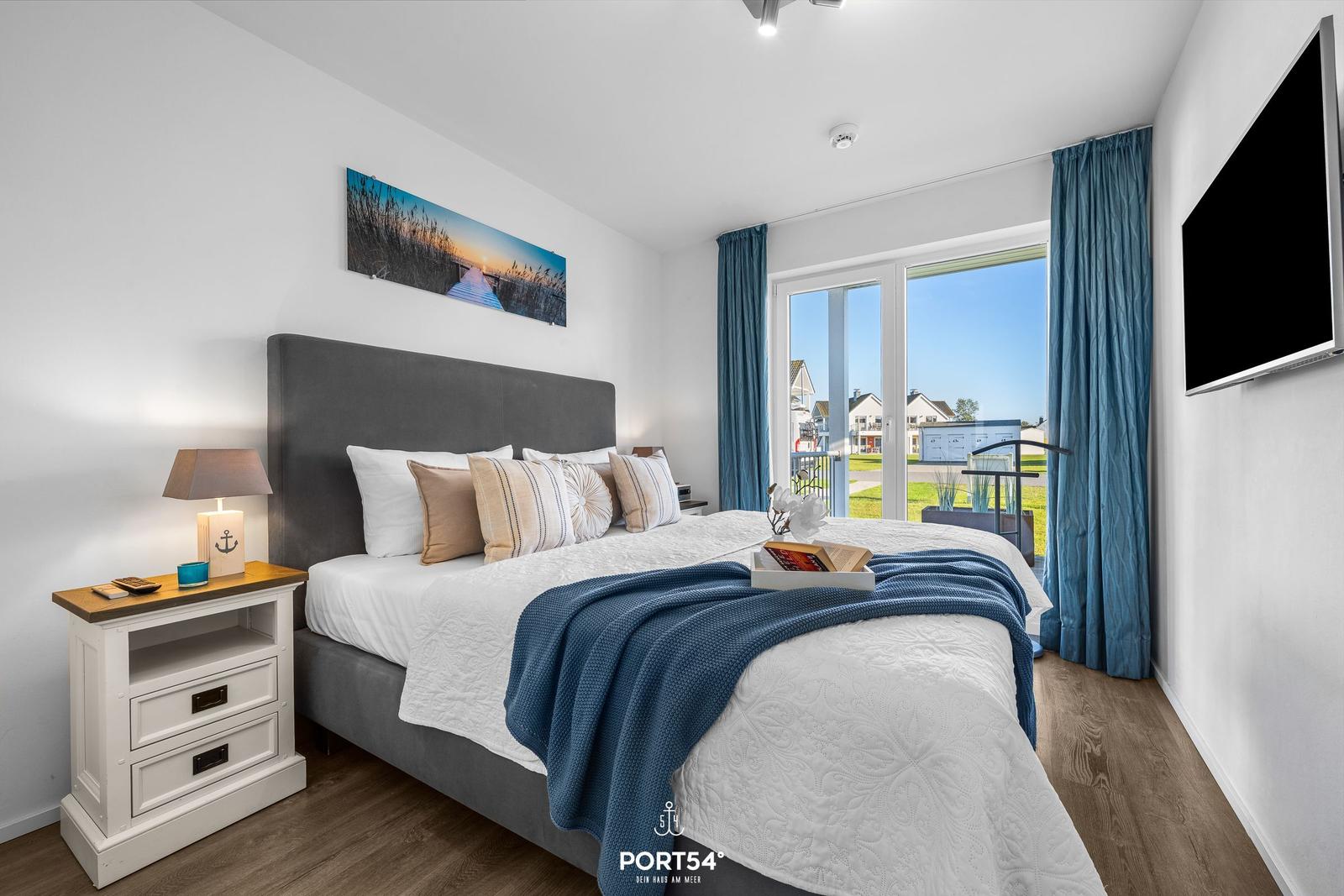 Schlafzimmer mit Bett, Nachttisch und TV. Blick auf Balkon und Garten.