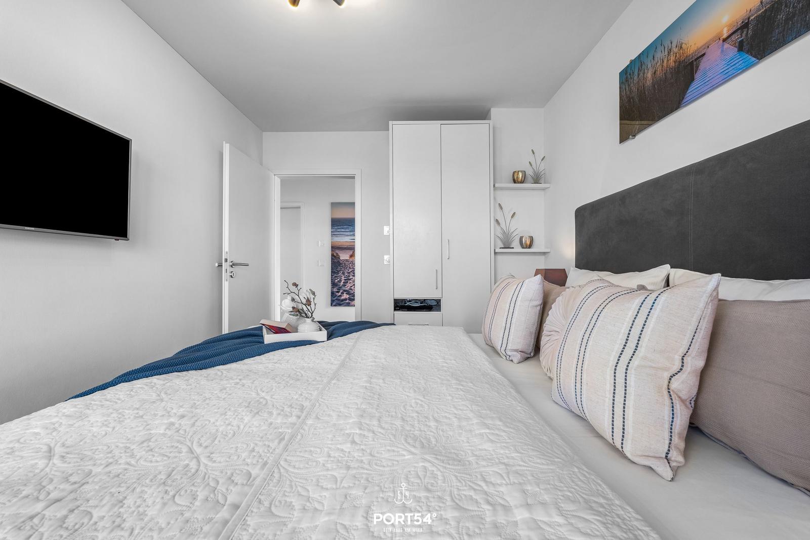 Schlafzimmer mit Bett, TV und Kleiderschrank. Wandbild zeigt Strand.