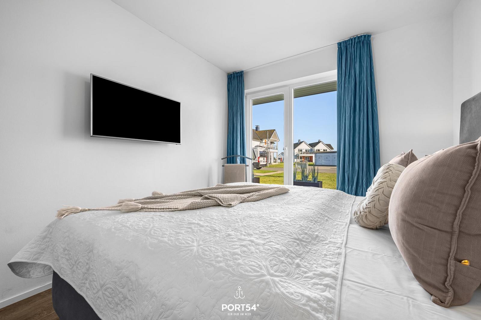 Schlafzimmer mit Bett, TV und Balkonblick.