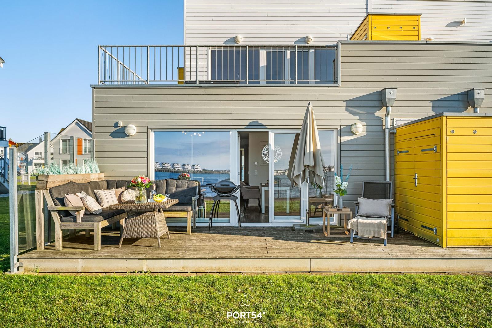 Terrasse mit Sitzgruppe, Grill und Blick aufs Wasser.