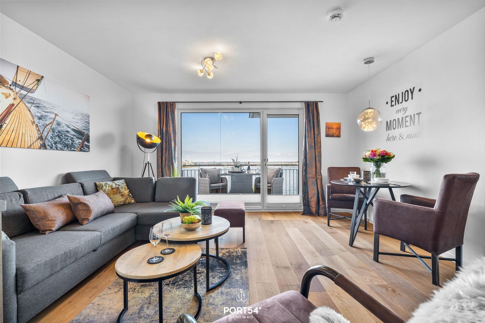 Wohnbereich mit Sofa, Esstisch und Balkonblick auf Wasser.