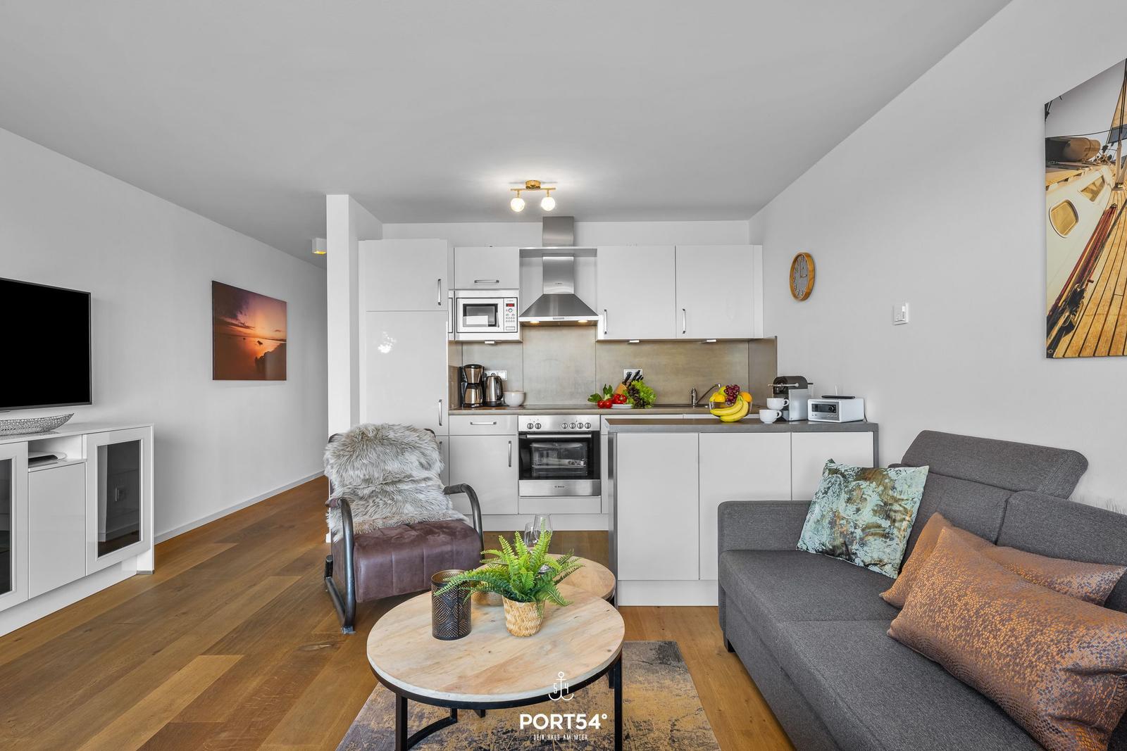 Wohnung mit Küche, Sofa und Fernseher. Holzboden und weiße Wände.