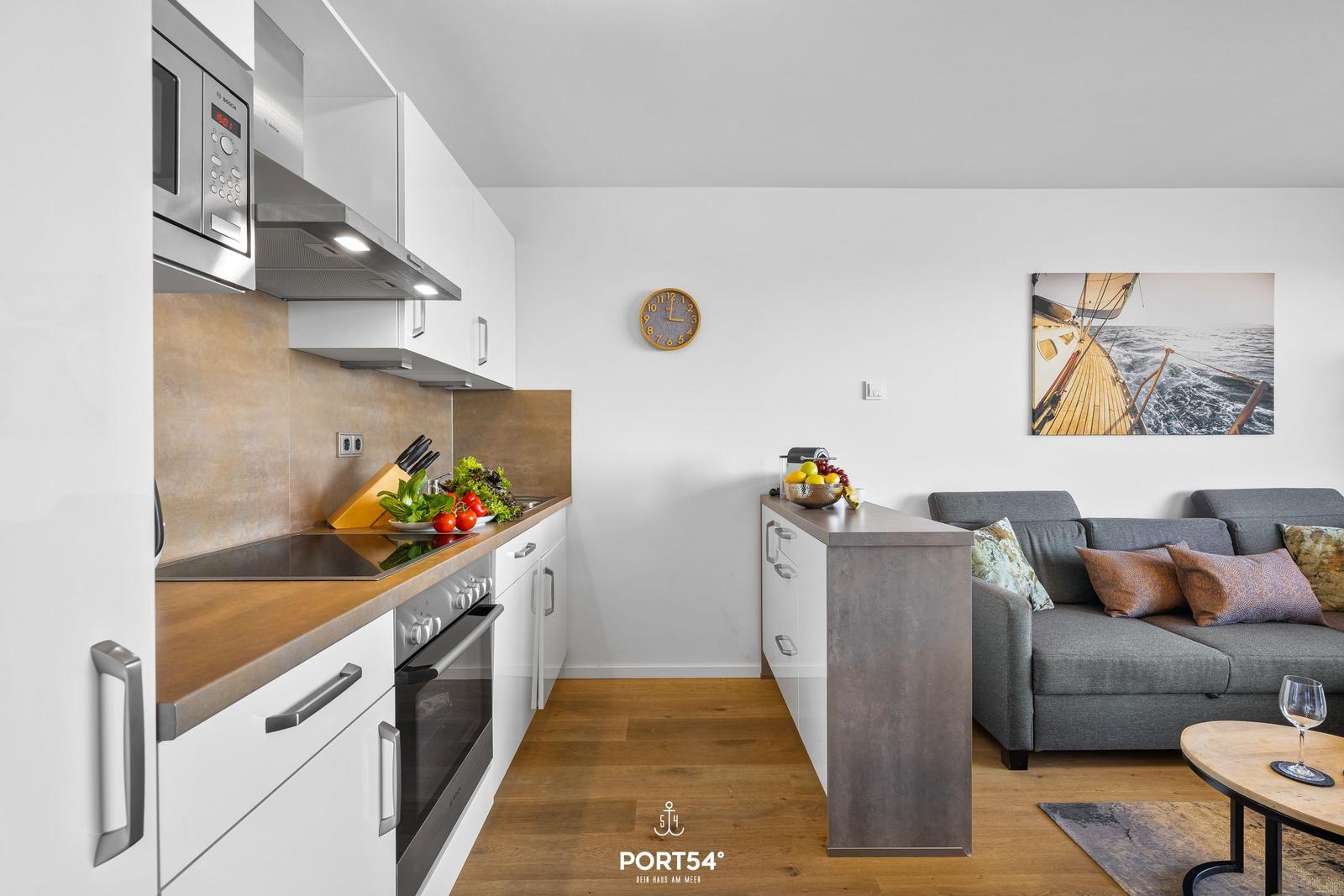 Küche mit Arbeitsfläche, Herd und Mikrowelle. Wohnbereich mit Sofa und Wandbild.