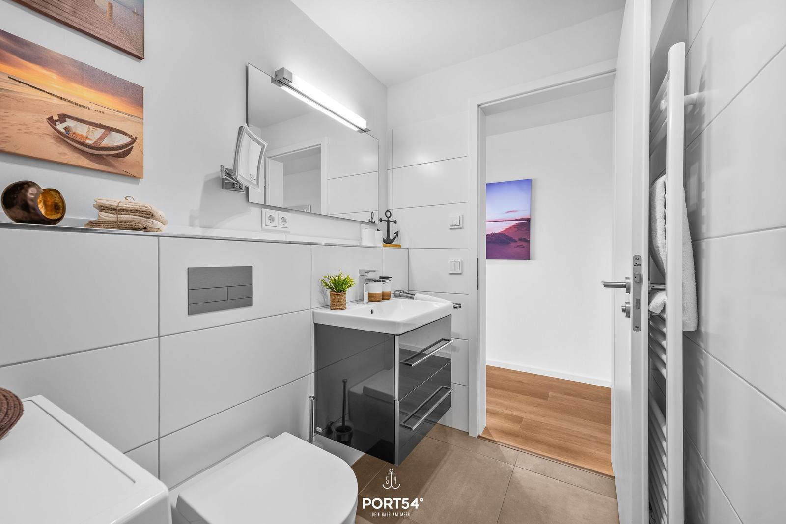 Badezimmer mit Waschbecken, Spiegel und Heizung. Wandbild zeigt Strand.