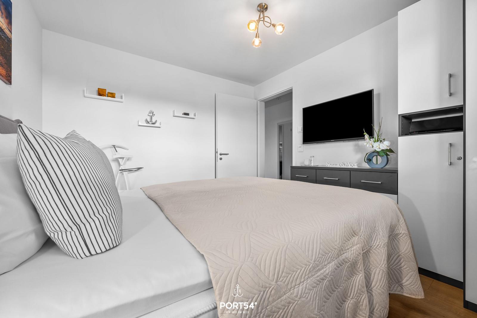 Schlafzimmer mit Bett, Fernseher und Schrank.