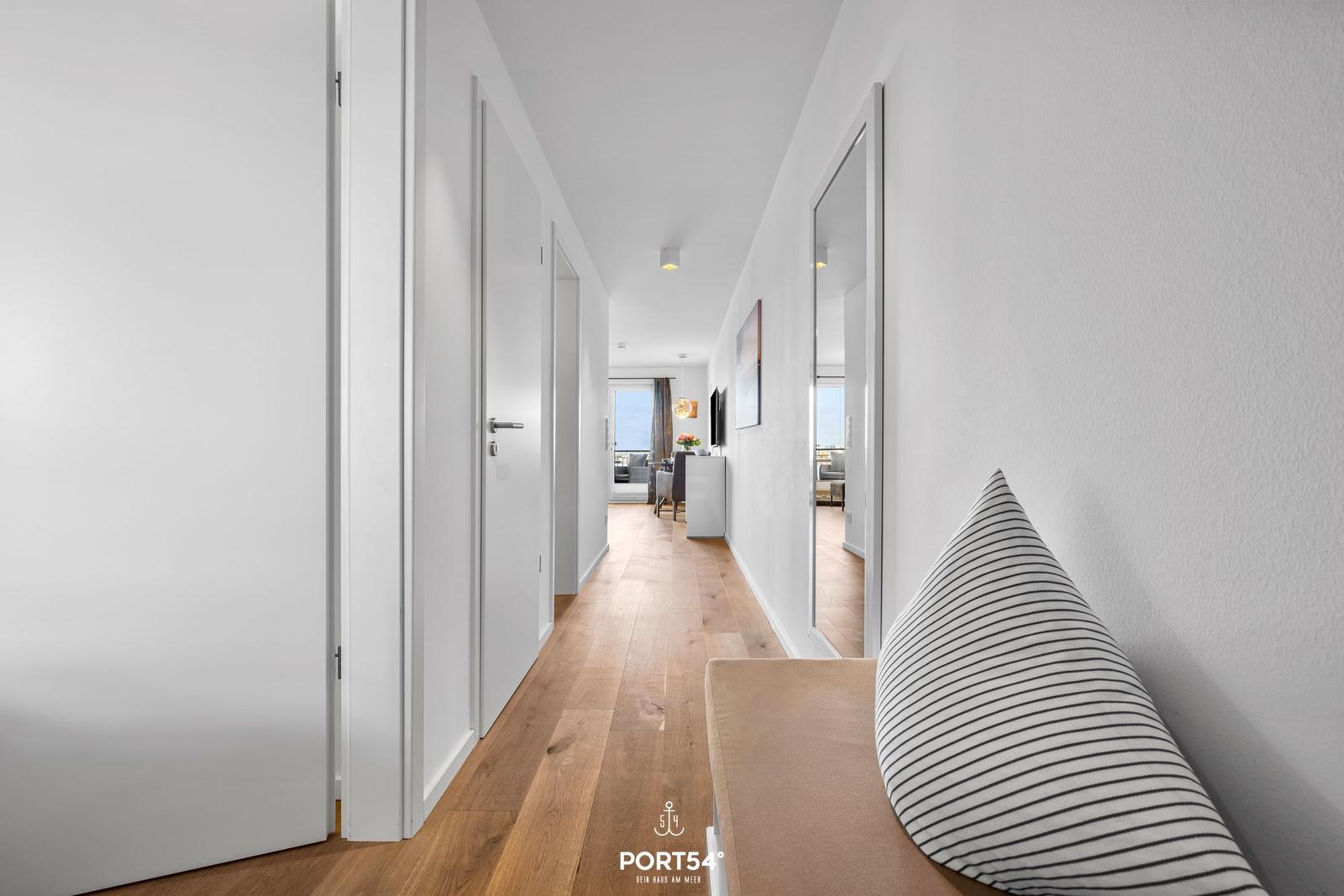 Flur mit Holzboden, weißen Wänden und Sitzbank mit Kissen.