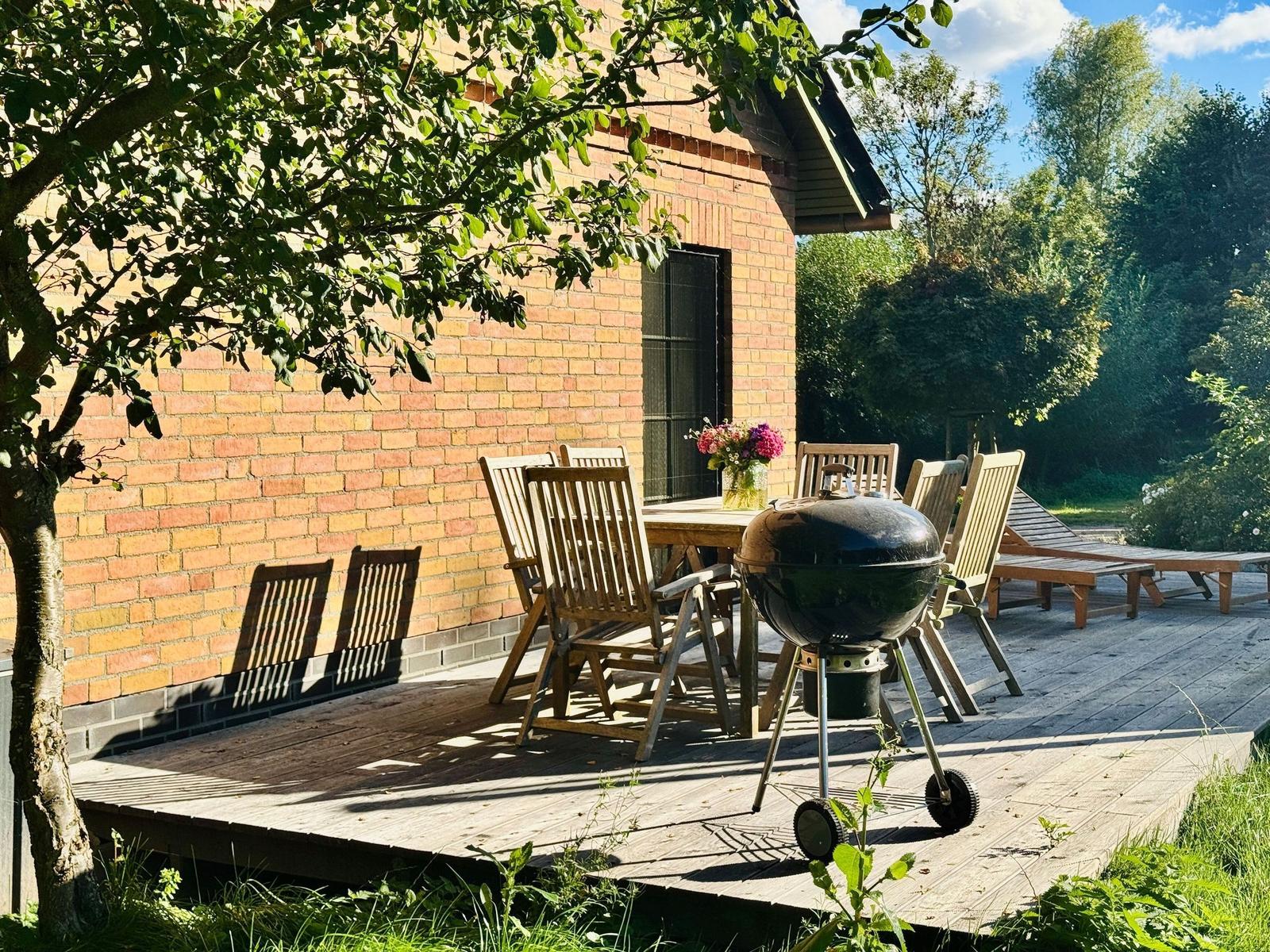 Terrasse mit Tisch, Stühlen und Grill neben Backsteinhaus.