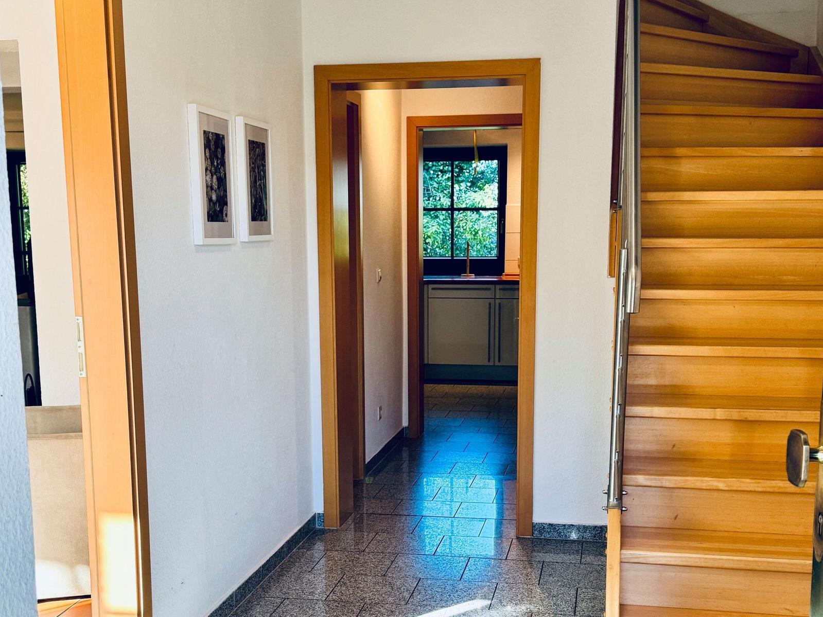Flur mit Holztreppe, Bildern an der Wand und Blick in die Küche.