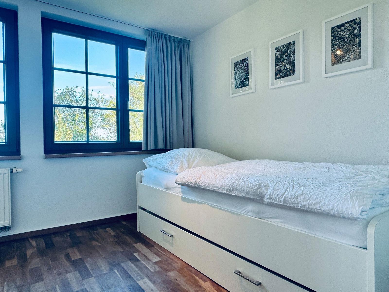 Schlafzimmer mit Bett, Fenster und Bildern an der Wand.