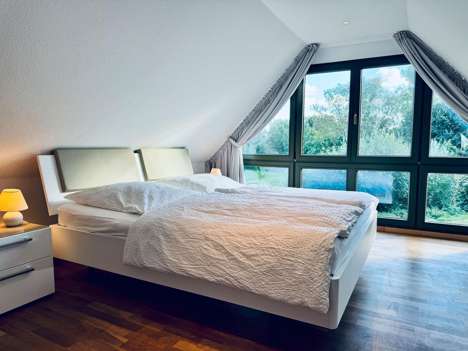 Schlafzimmer mit Doppelbett, großem Fenster und Holzboden.