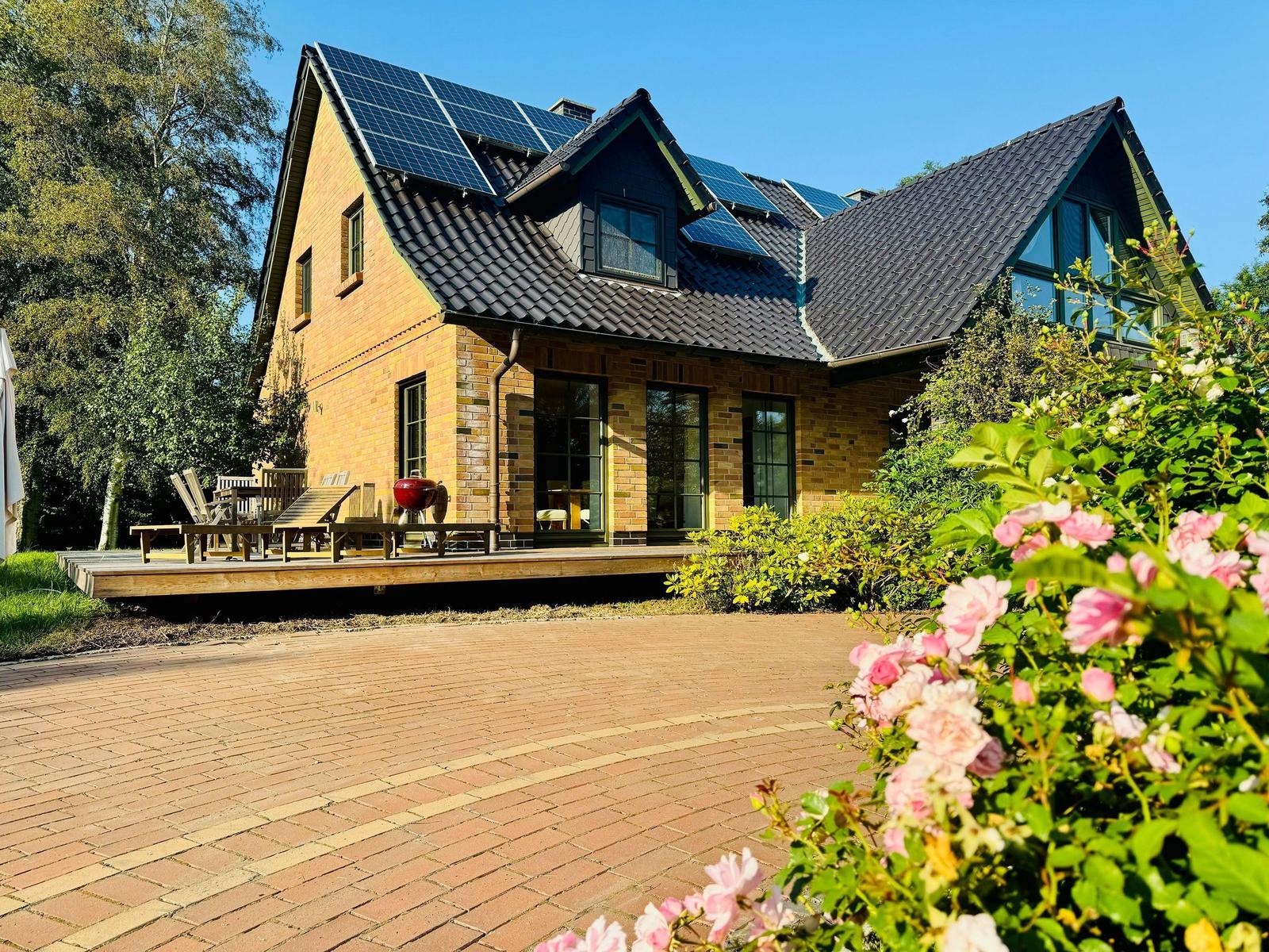 Haus mit Solaranlage, Terrasse und Blumenbeet im Vordergrund.