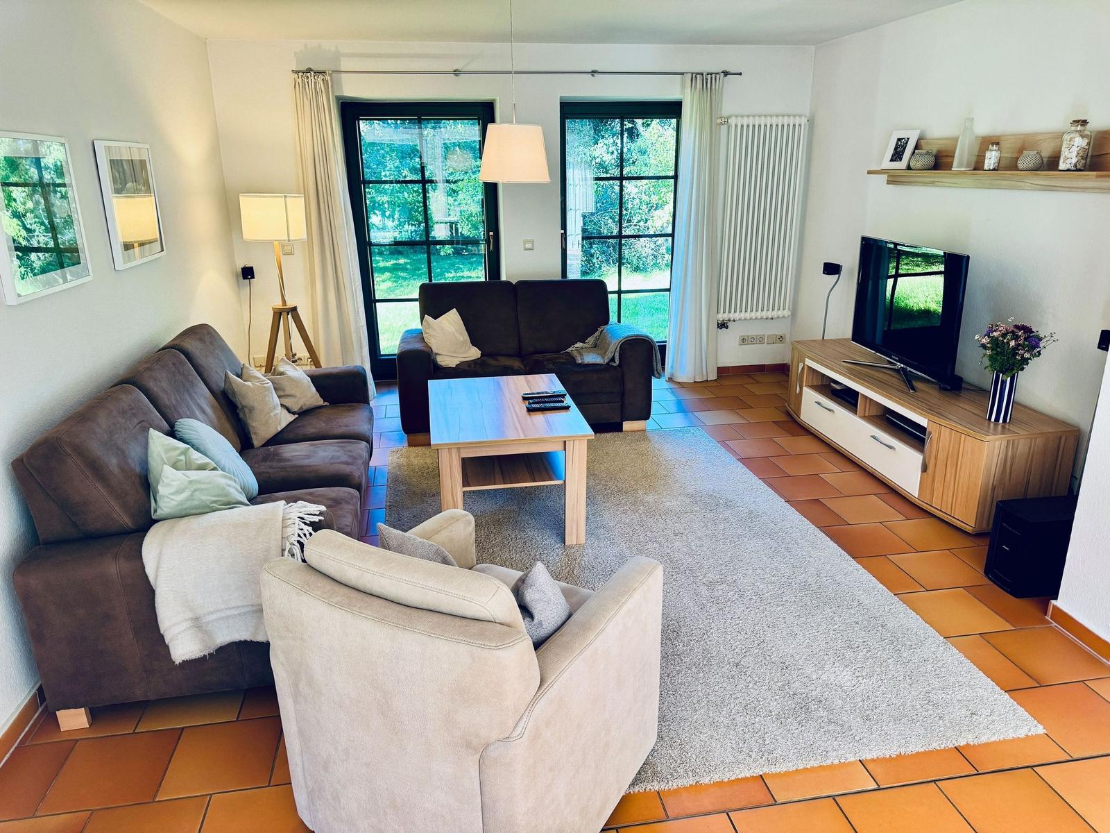 Wohnzimmer mit Sofa, Sessel, Couchtisch und Fernseher.