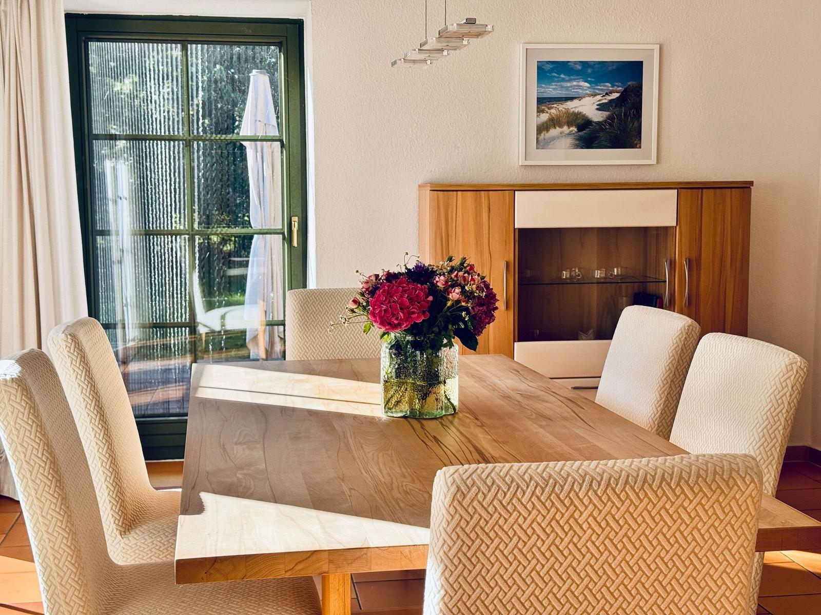 Esstisch mit sechs Stühlen und Blumen im Esszimmer. Durchgang zur Terrasse.