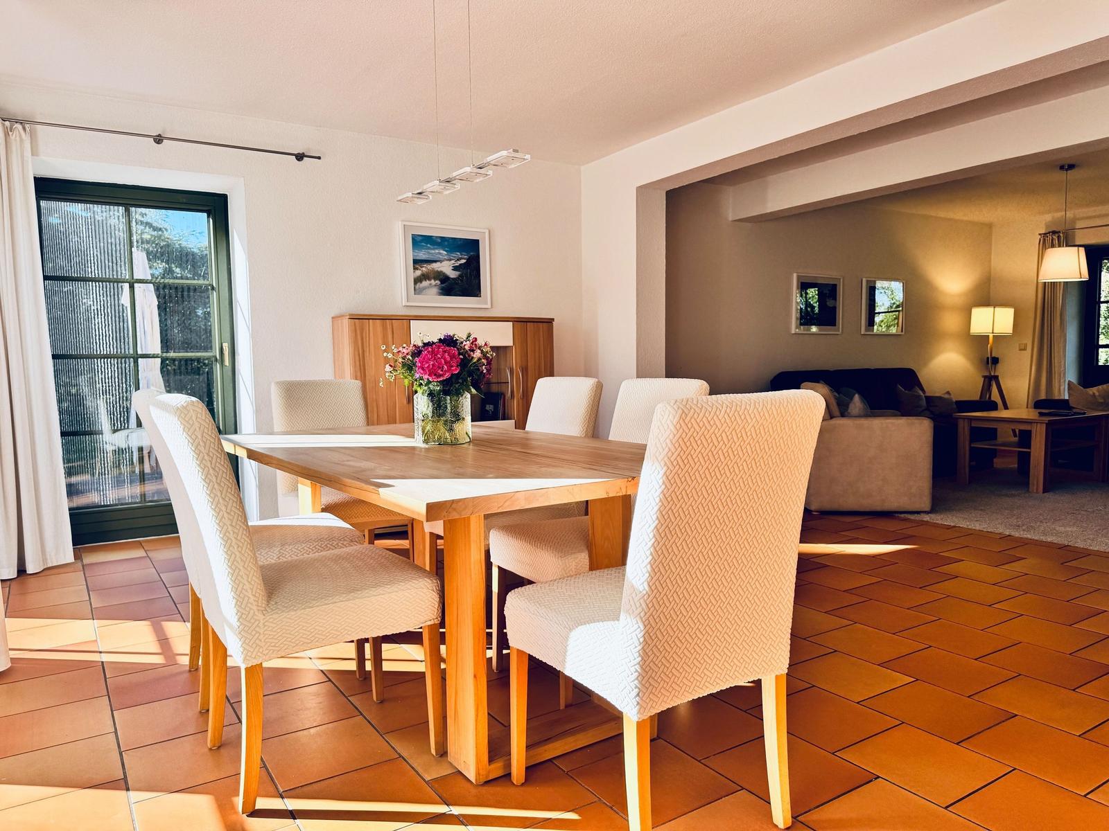 Essbereich mit Holztisch und Stühlen. Wohnbereich im Hintergrund mit Sofa und Tisch.