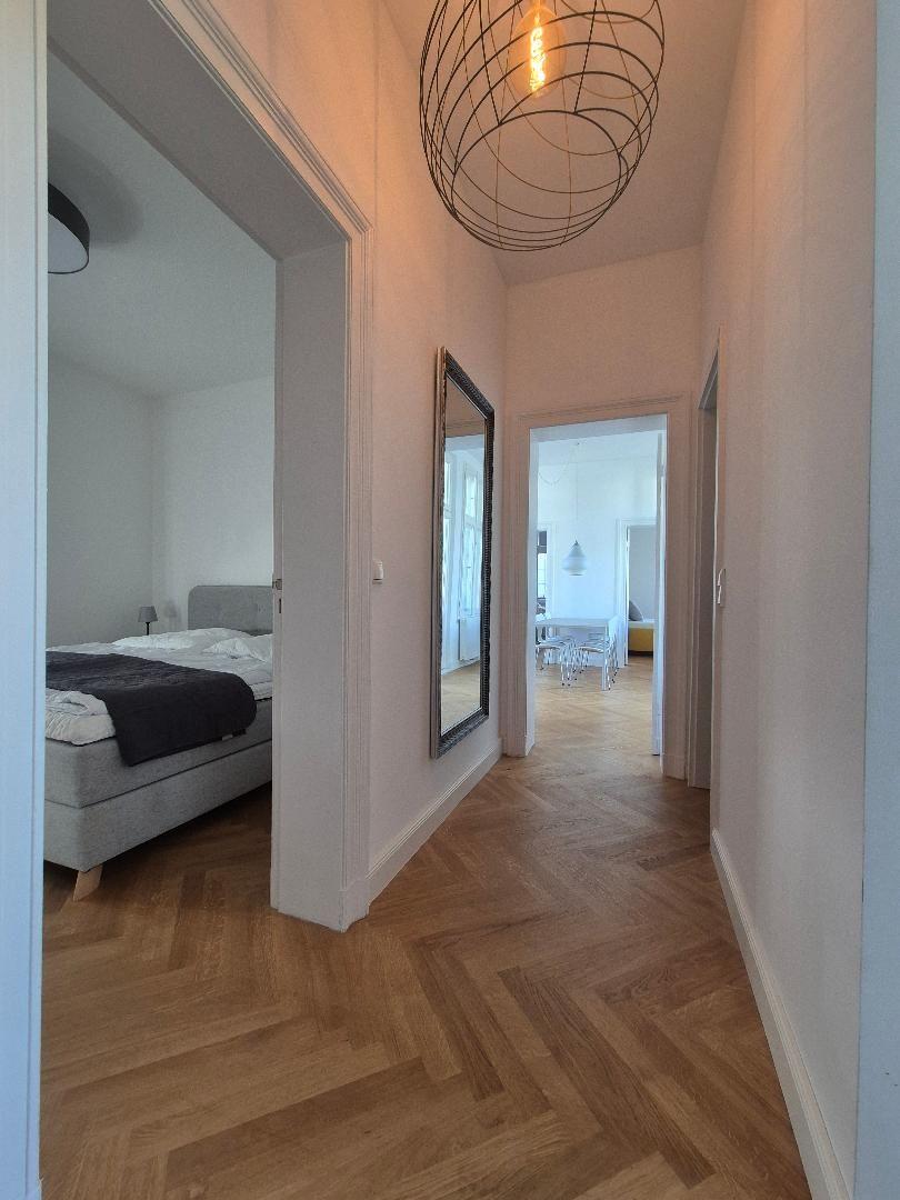 Flur mit H Stockboden, Spiegel und Schlafzimmer im Hintergrund.