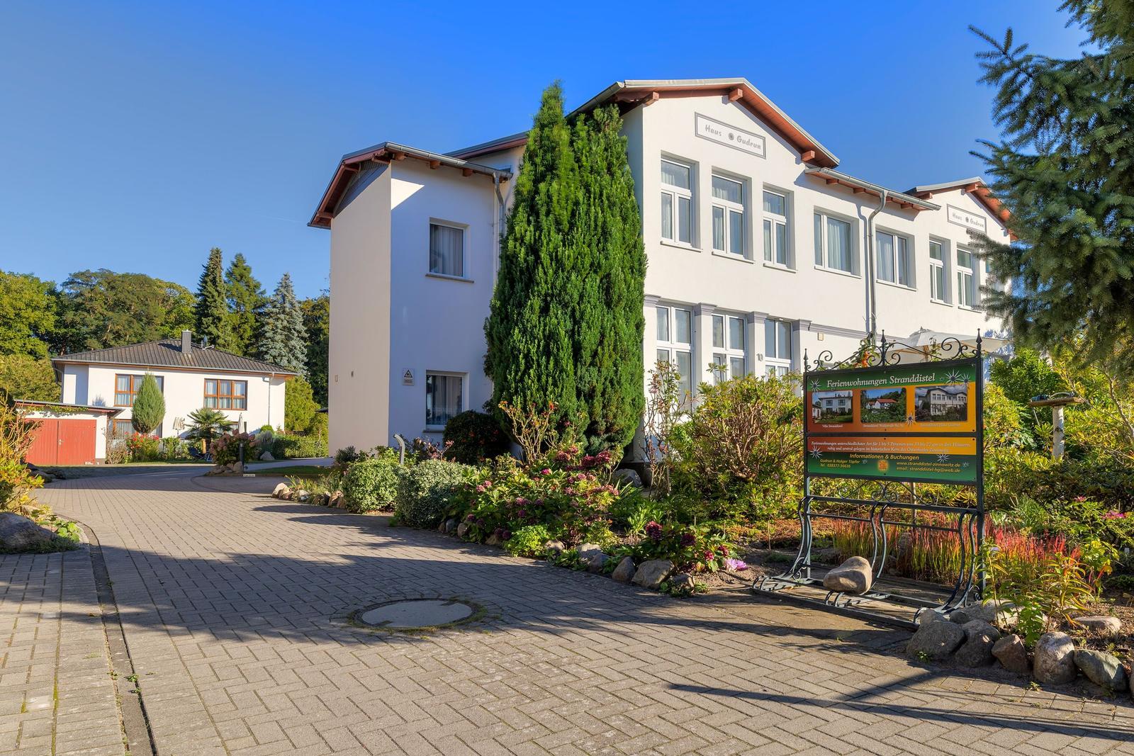 Weiße Ferienhausanlage mit gepflastertem Weg und Garten. Schild mit Informationen.