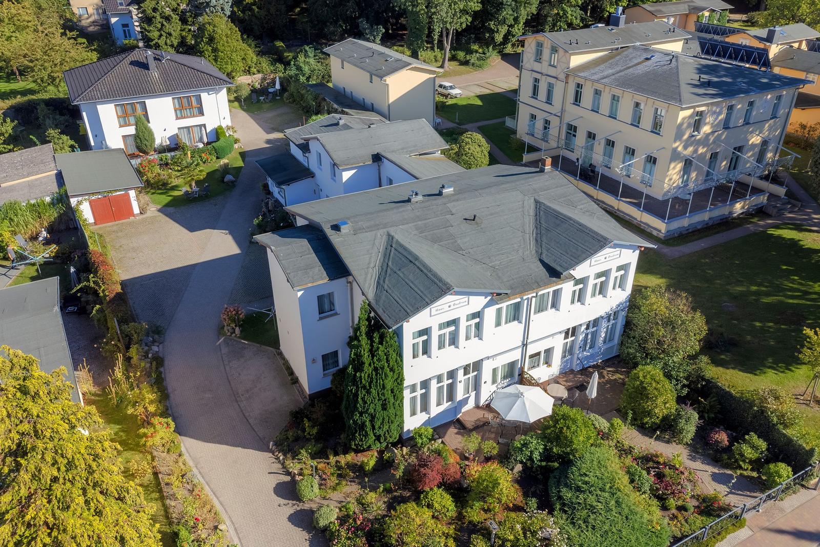 Haus mit Garten und Terrasse. Umgeben von Bäumen und weiteren Gebäuden.