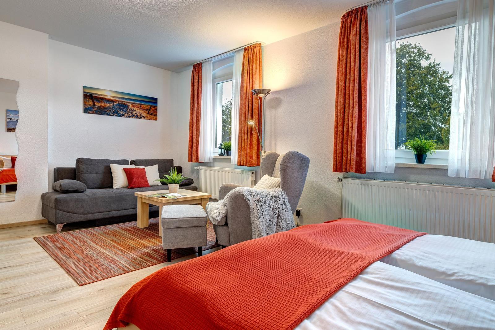 Ein Schlafzimmer mit Sofa, Sessel und großem Fenster mit Blick auf Bäume.