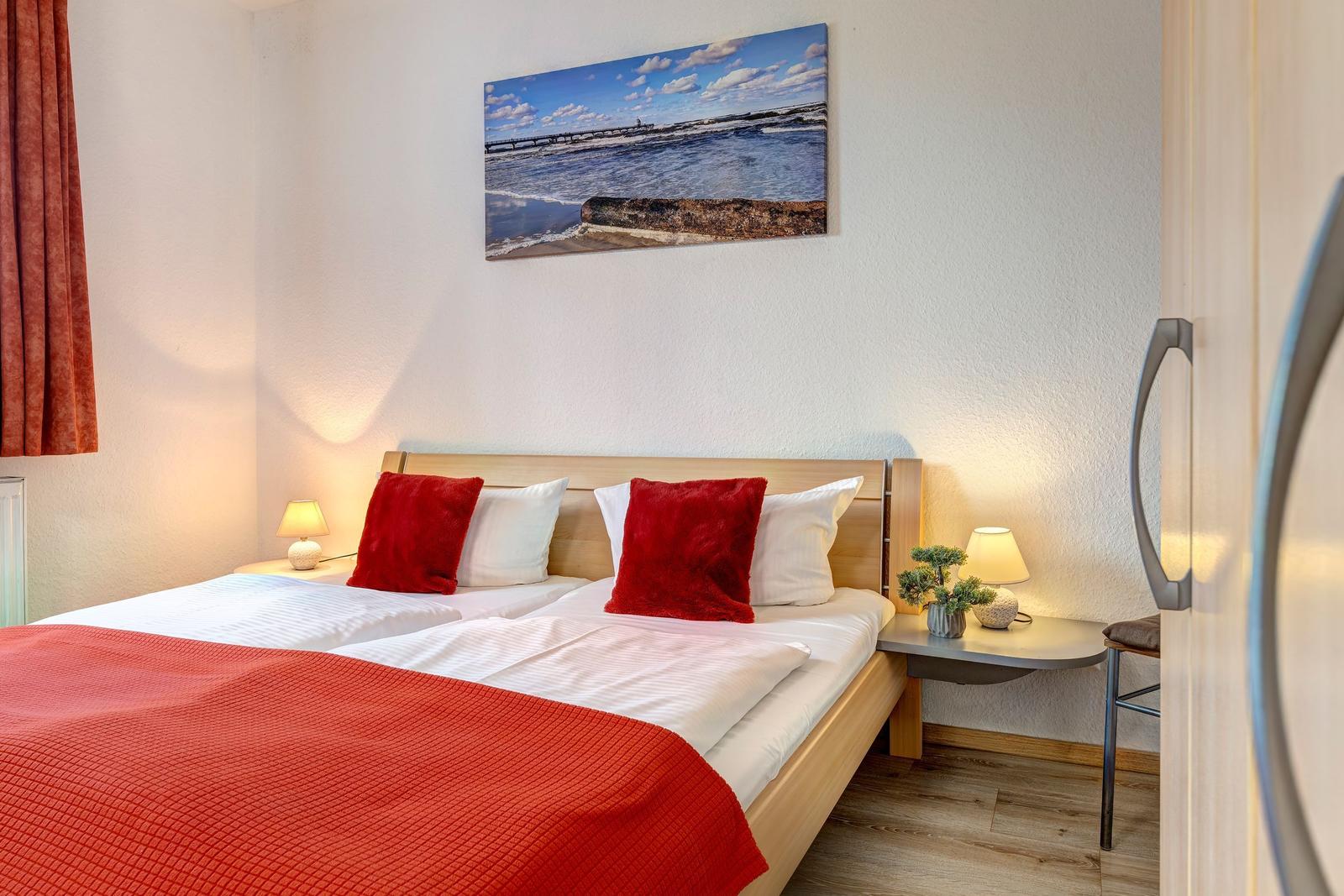 Schlafzimmer mit Doppelbett, roter Decke und Wandbild an der Wand.