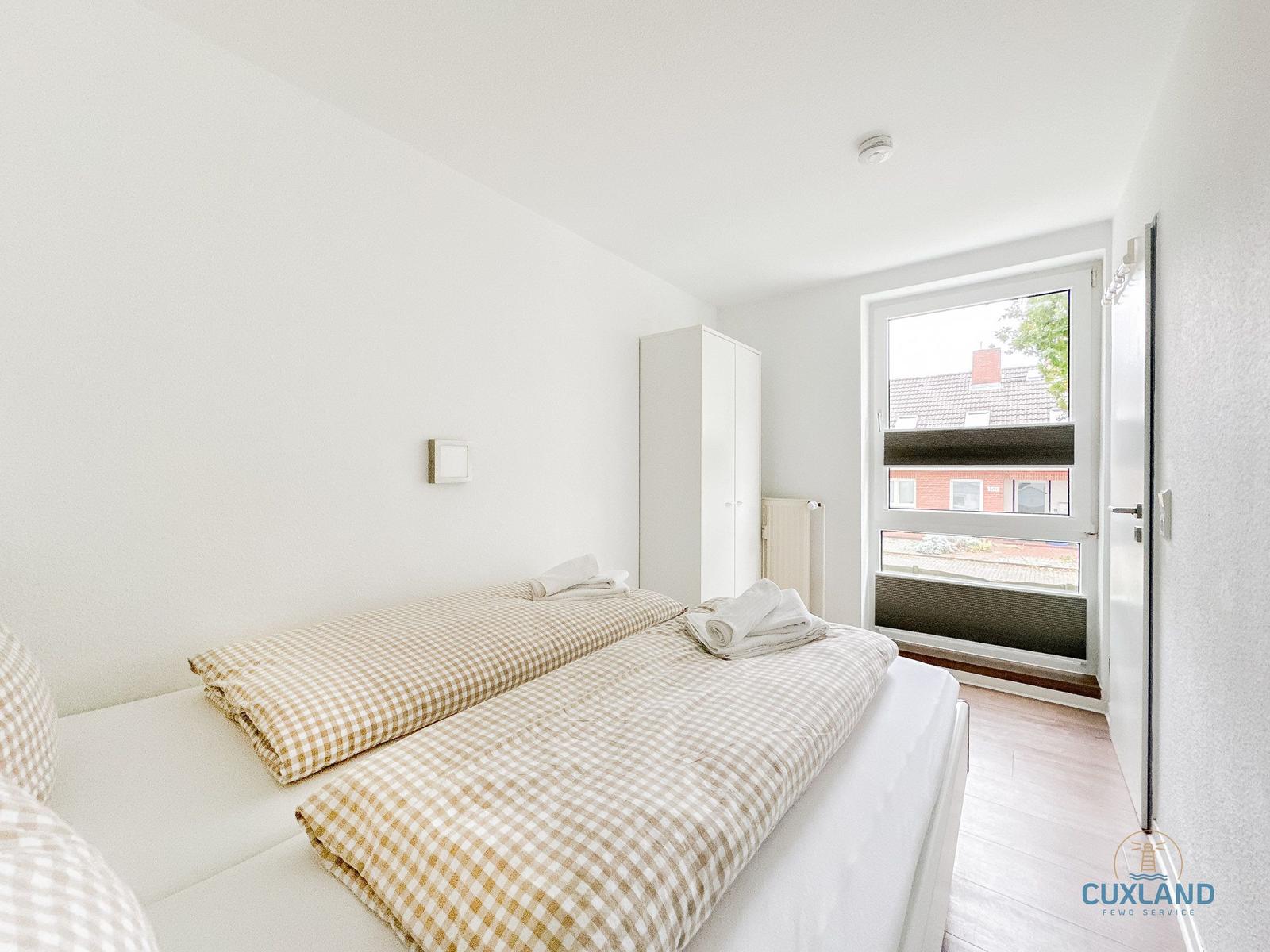 Schlafzimmer mit Bett, Kleiderschrank und Fenster. Bett mit kariertem Bettzeug.