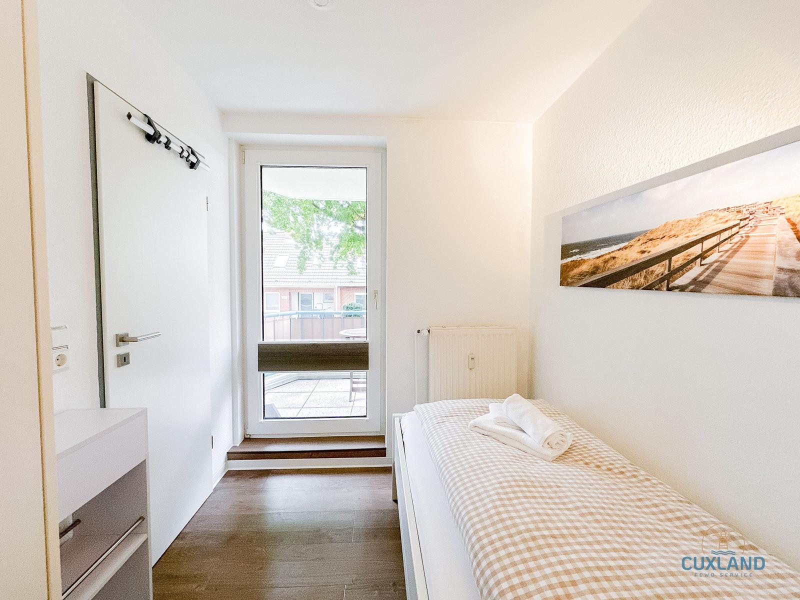 Schlafzimmer mit Bett, Tür und Fenster zur Terrasse.