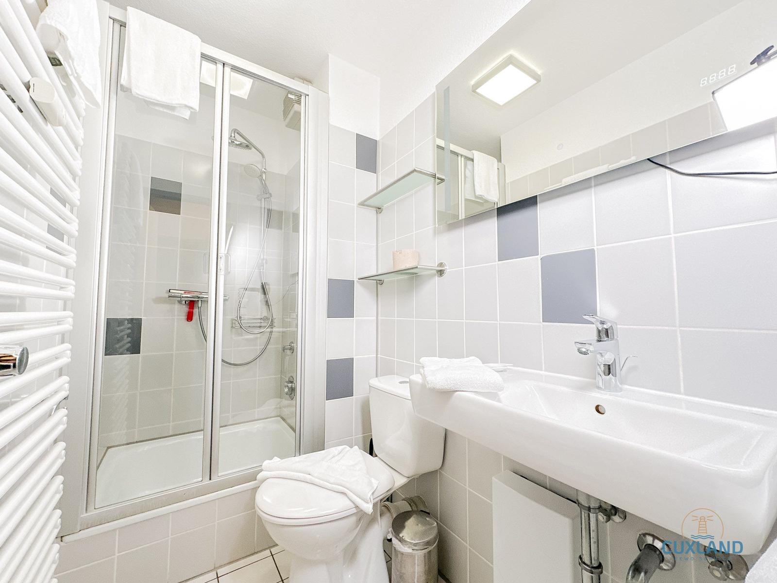 Badezimmer mit Dusche, Waschbecken und Toilette. Weiße Fliesen und Spiegelschrank.
