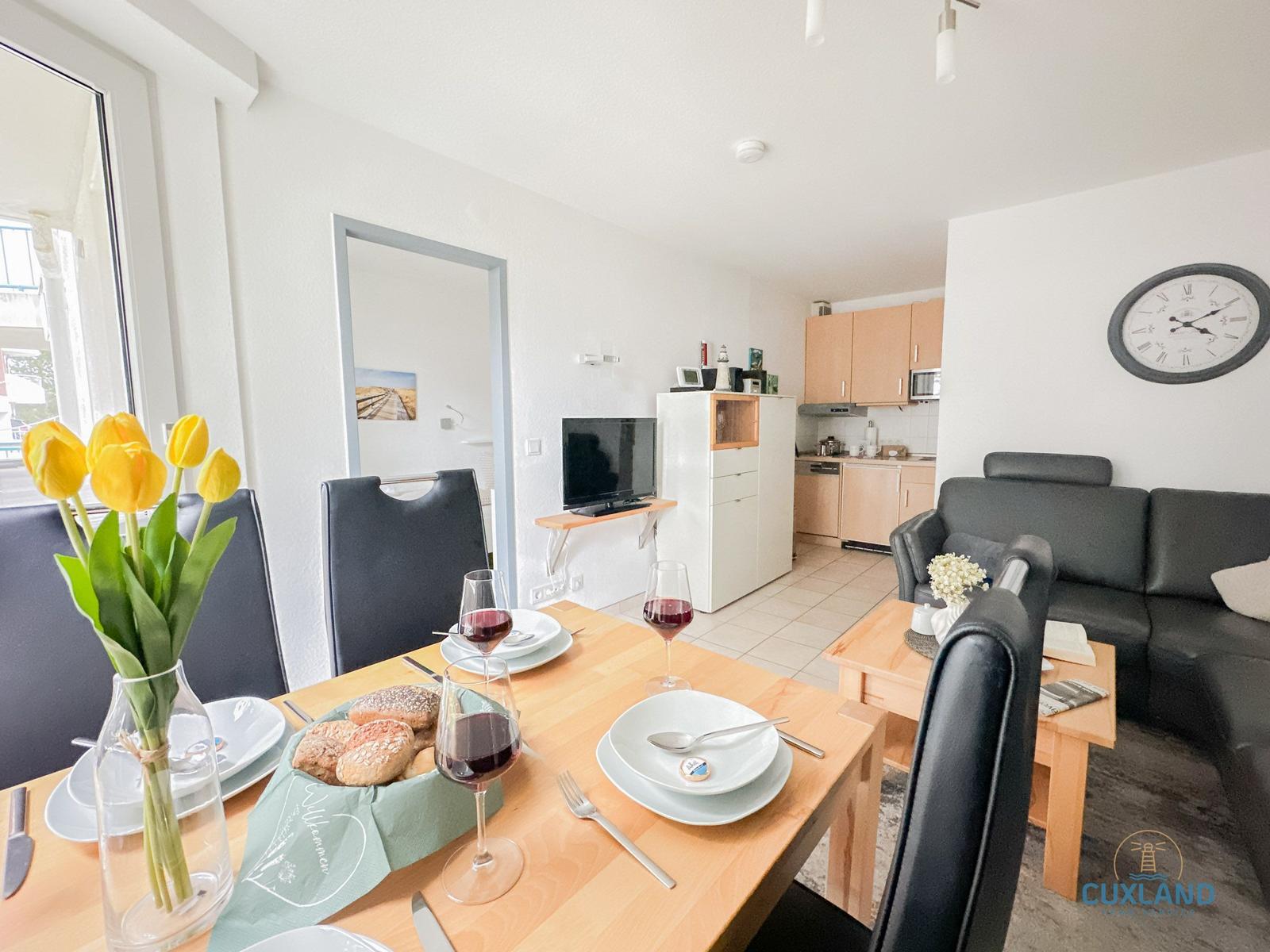 Esstisch mit Wein und Brot, Wohn- und Küchenbereich mit Sofa und Küchenschränken.