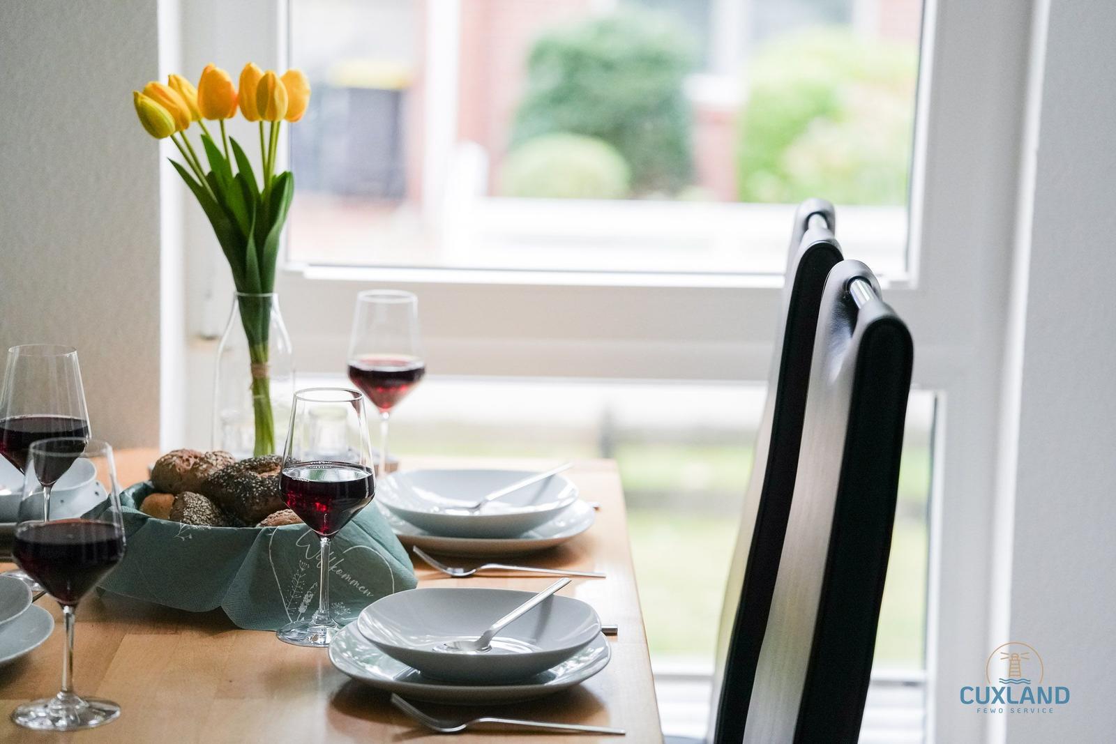 Tisch gedeckt mit Wein, Brot und Tulpen vor Fenster