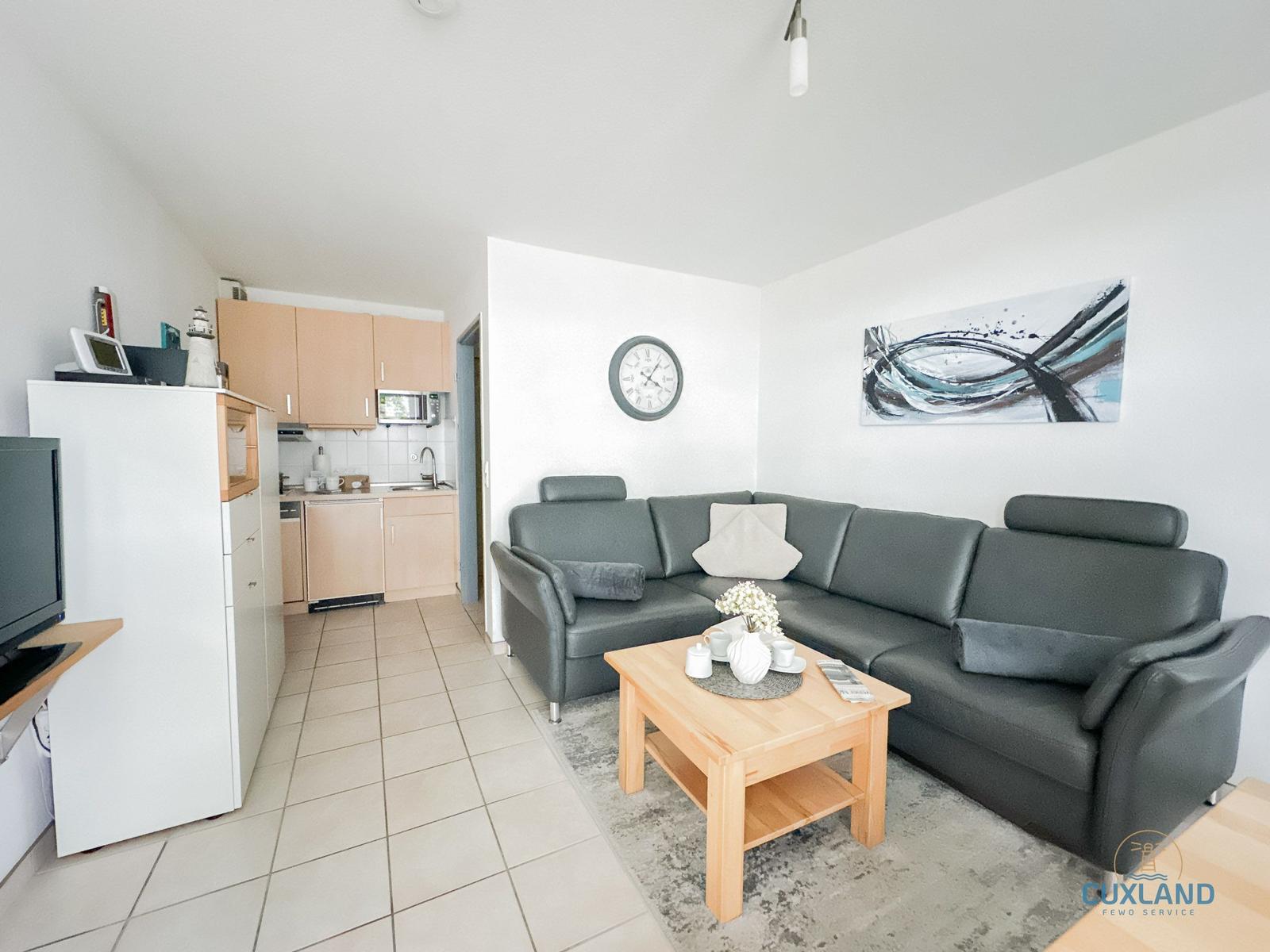 Wohnküche mit grauem Sofa, Holztisch und Küchenschränken.