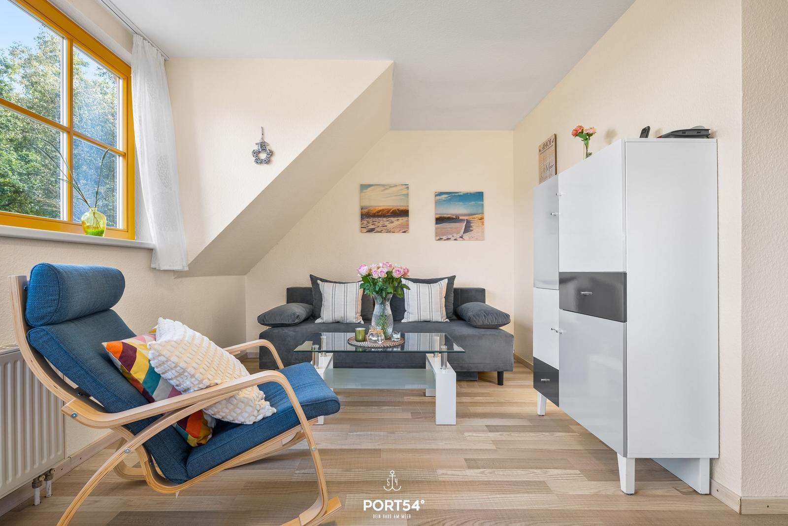 Wohnzimmer mit Sofa, Sessel und Glas-Tisch unter Dachschrägen.