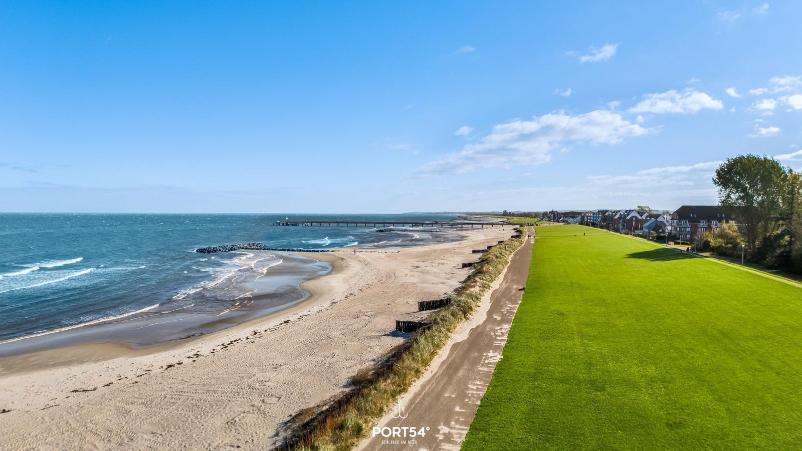 Strand mit grünem Rasen und Blick auf das Meer unter blauem Himmel.
