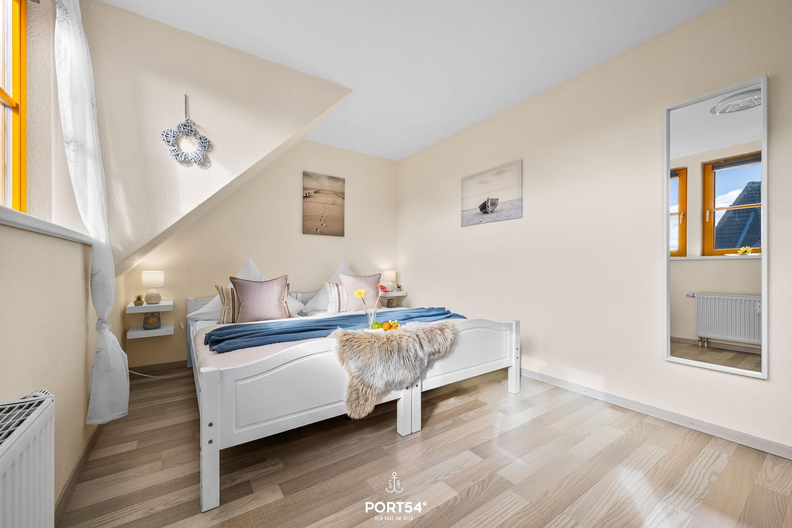 Schlafzimmer mit weißem Bett, Holzboden und Spiegeln an der Wand.