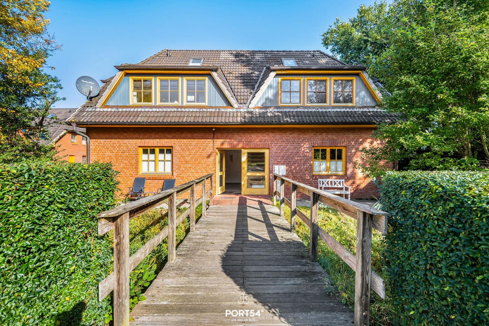 Haus mit Holzbrücke, roten Ziegel und gelben Fensterrahmen.
