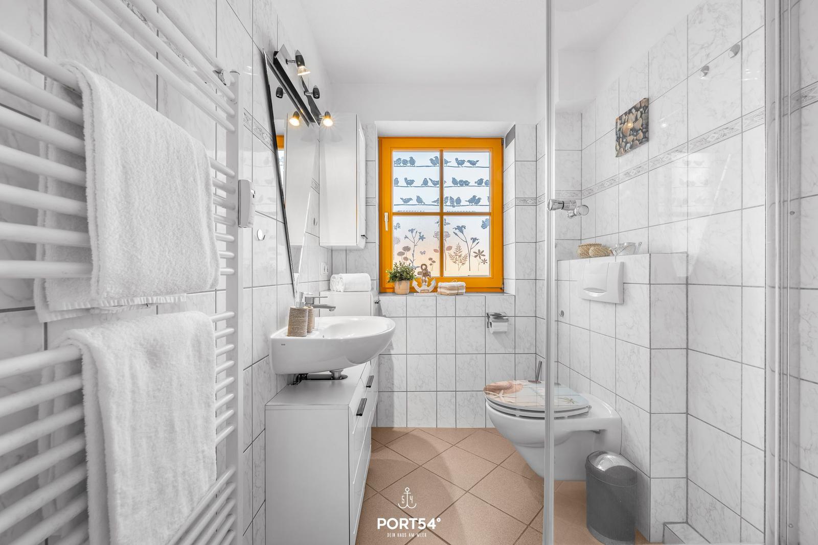 Badezimmer mit Dusche, Toilette und Waschbecken. Fenster mit Vogelmotiv.