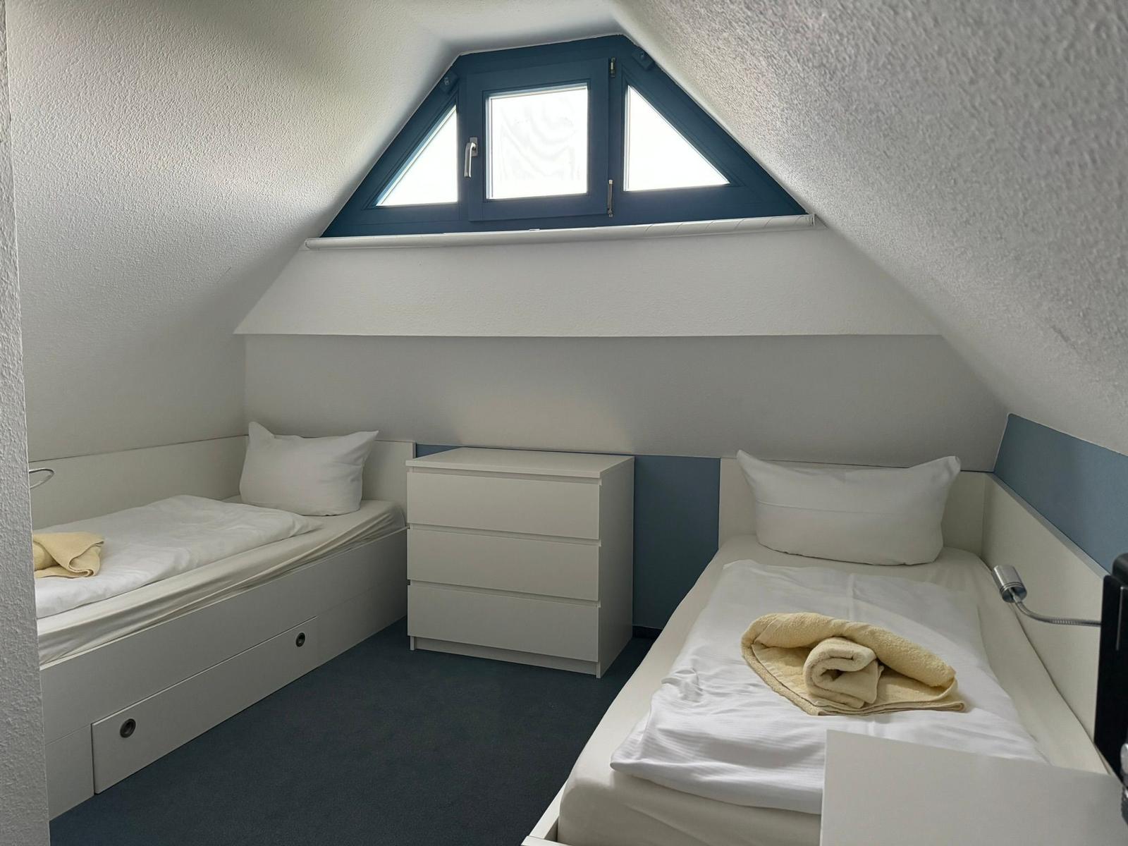 Zimmer mit zwei Einzelbetten, Schrank und Dachfenster.