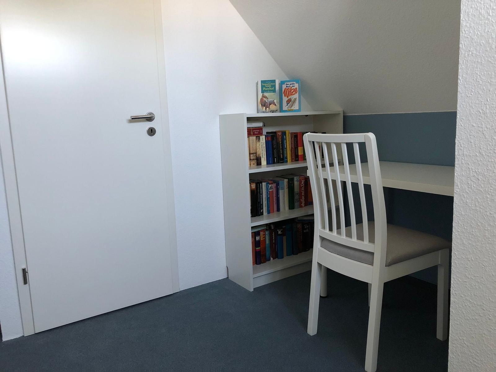 Eckplatz mit Schreibtisch, Stuhl und Bücherregal an der Wand.