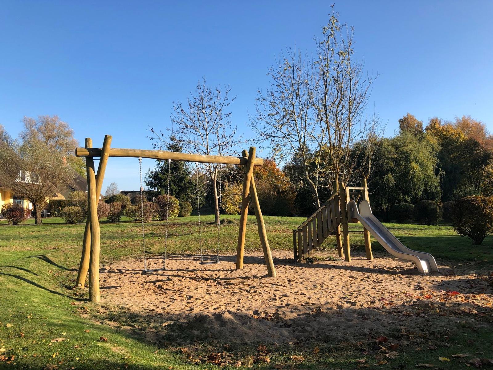 Kinder-Spielplatz mit Schaukel und Rutsche auf Sandfläche im Garten
