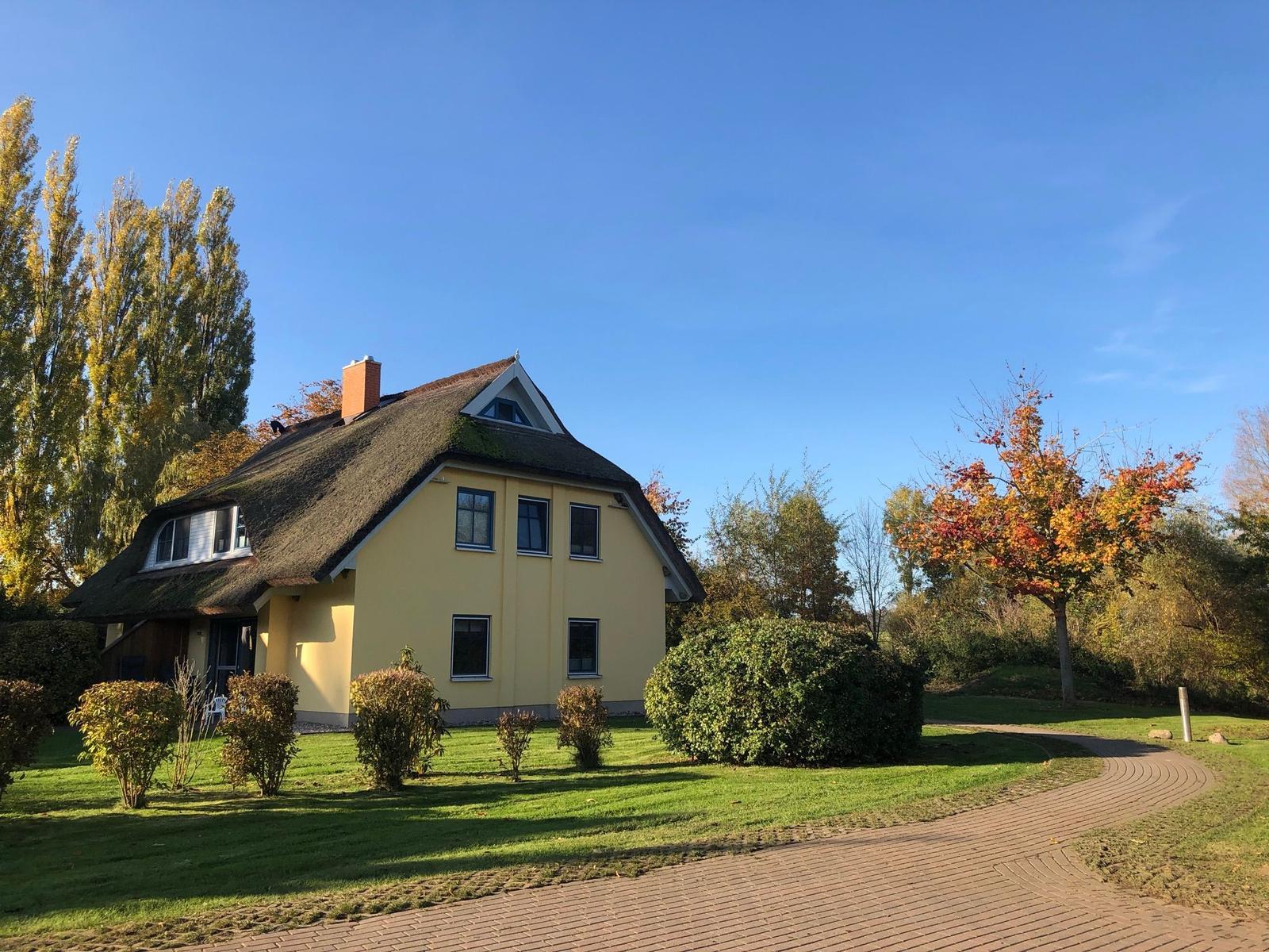 Ein gelbes Haus mit Strohdach, umgeben von Grün und Bäumen unter blauem Himmel.