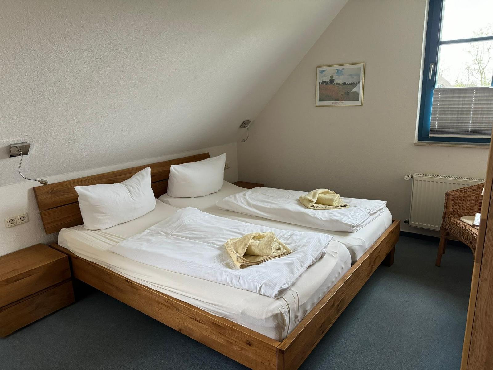 Doppelbettzimmer mit Holzbett, Fenster und Wandbild.