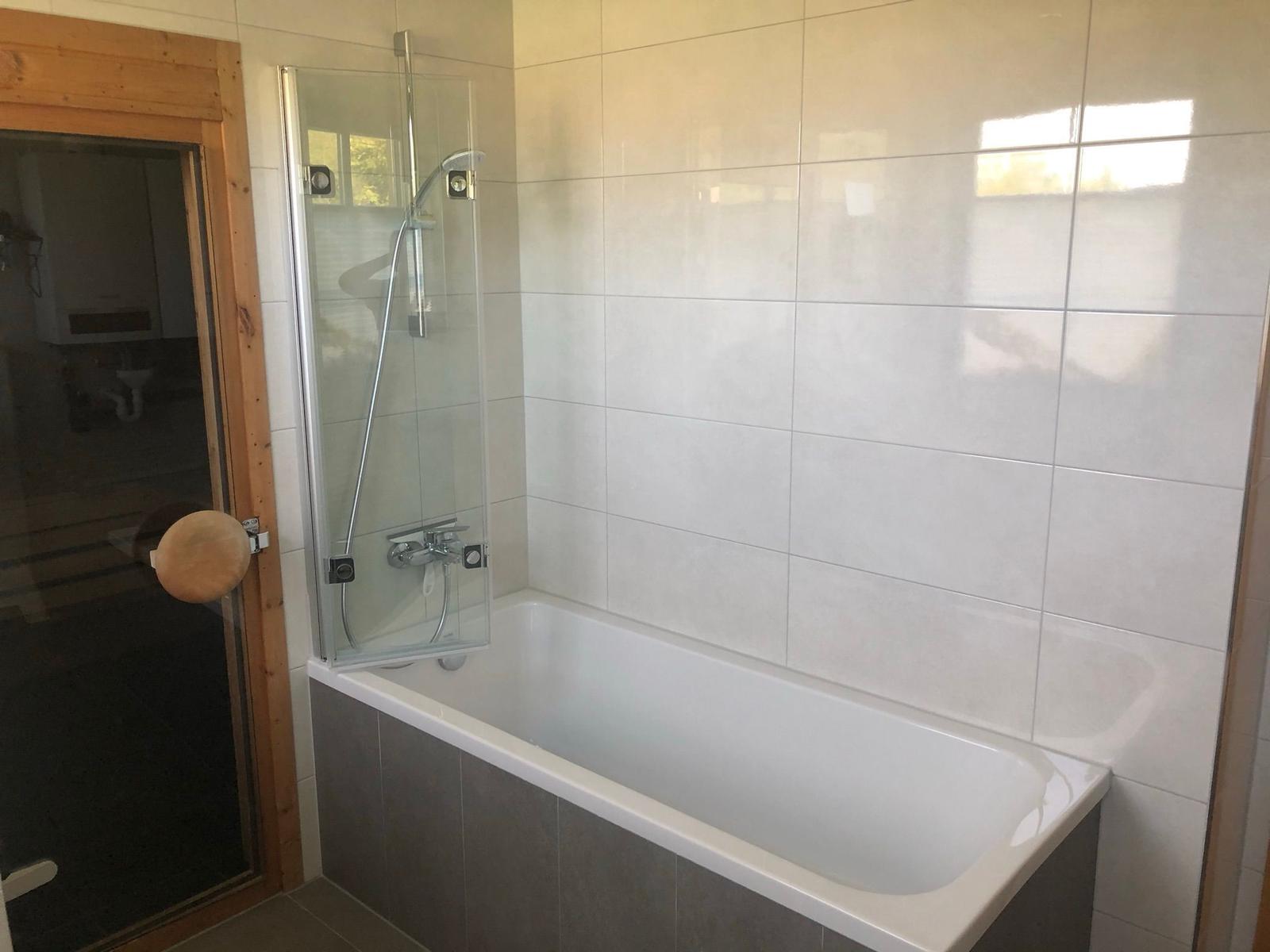 Bad mit Badewanne und Duschkabine, weiße Fliesen, Holztür